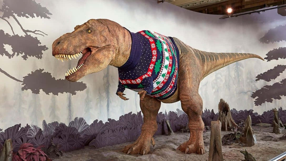 t-rex 桌布 壁紙 — 一個逼真的暴龍模型在博物館的立體模型中穿著節日紅綠藍圖案毛衣，背景有彩繪樹木和紫色樹葉。