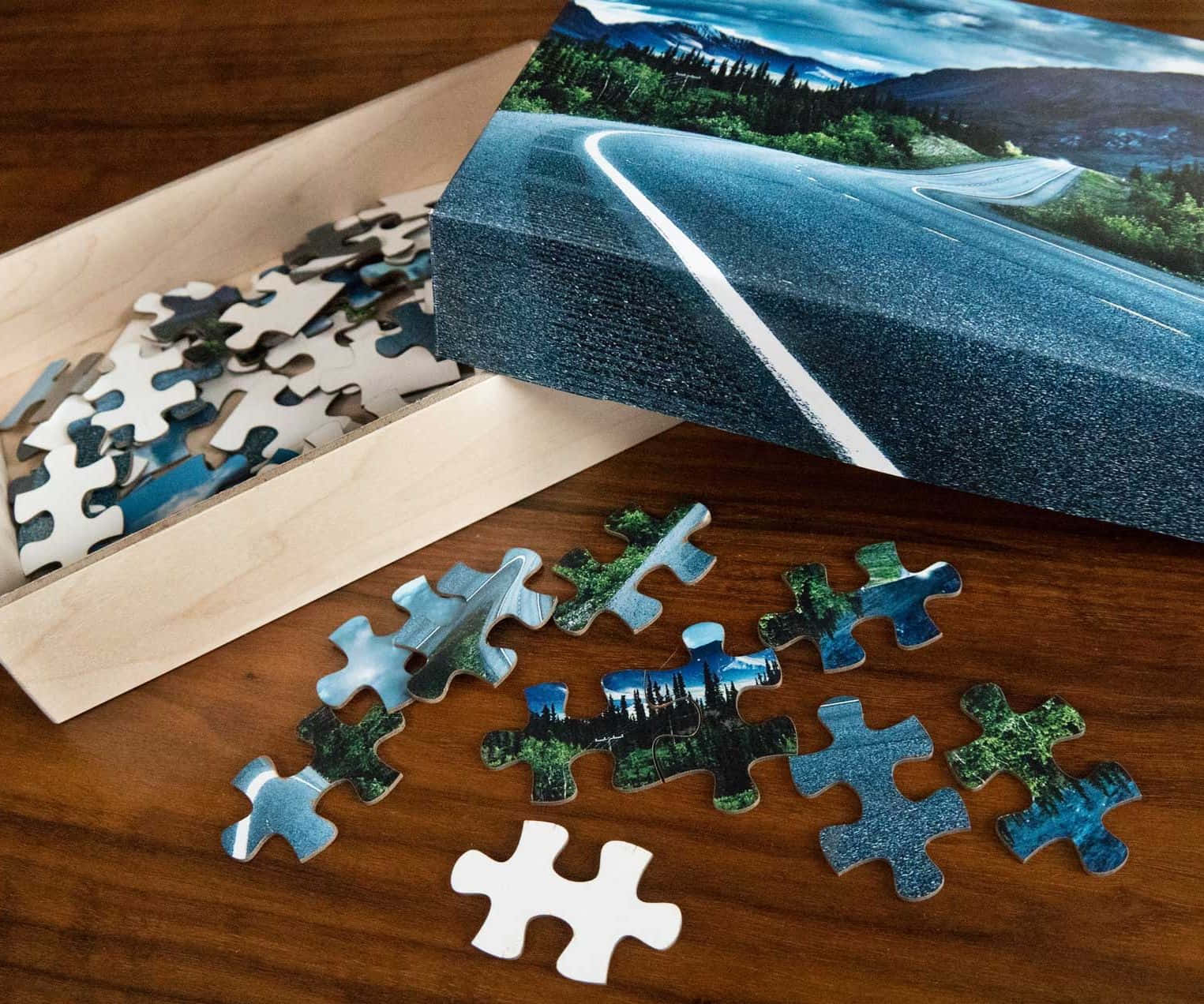 Puzzle 桌布 壁紙 — 一個部分組裝的拼圖，展示蜿蜒的山路，碎片散落在木桌上。