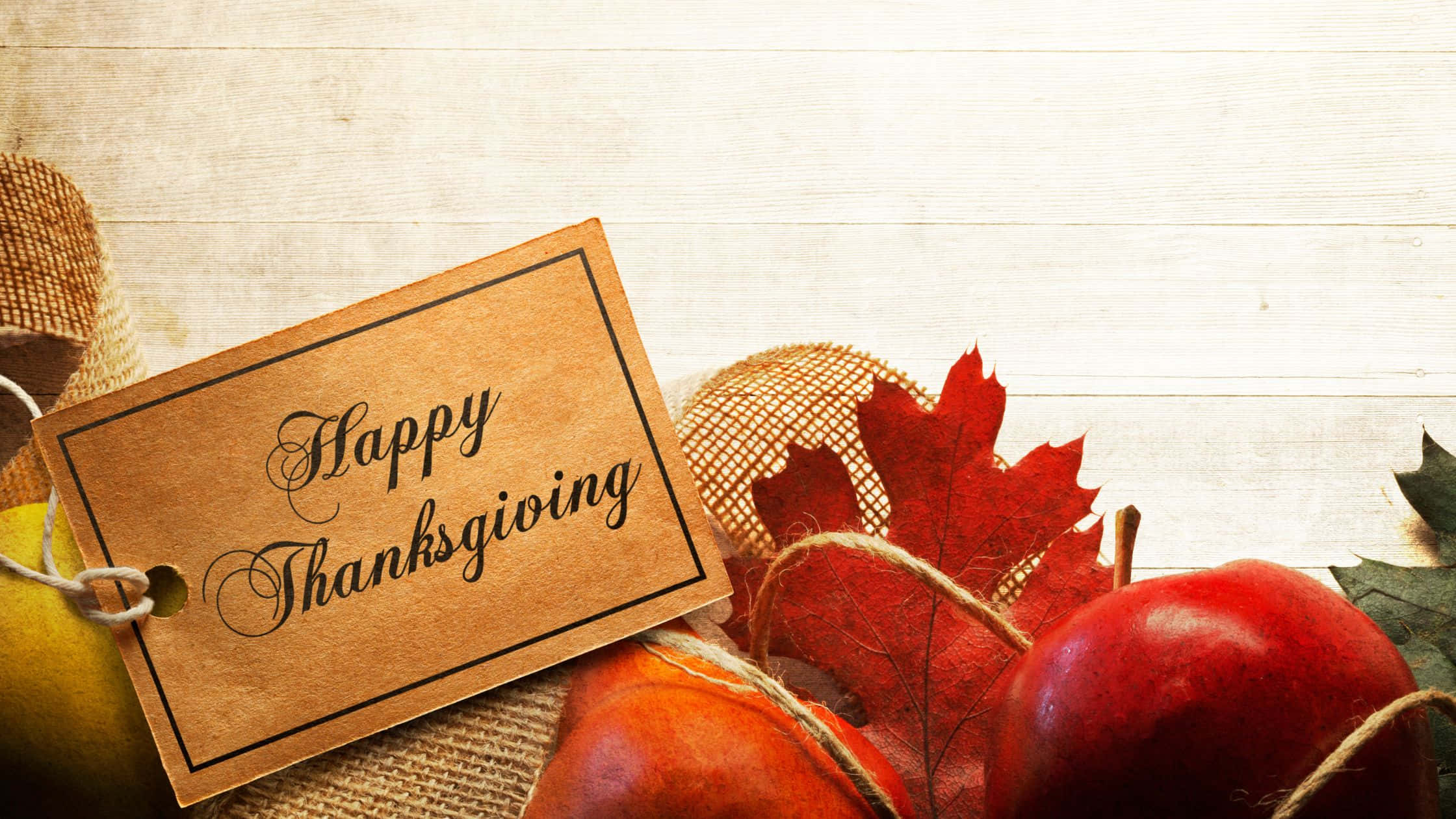 Thanksgiving Desktop 桌布 壁紙 — 一個鄉村風格的「感恩節快樂」標籤放在經風化的木質表面上，旁邊是鮮紅的蘋果和秋葉。