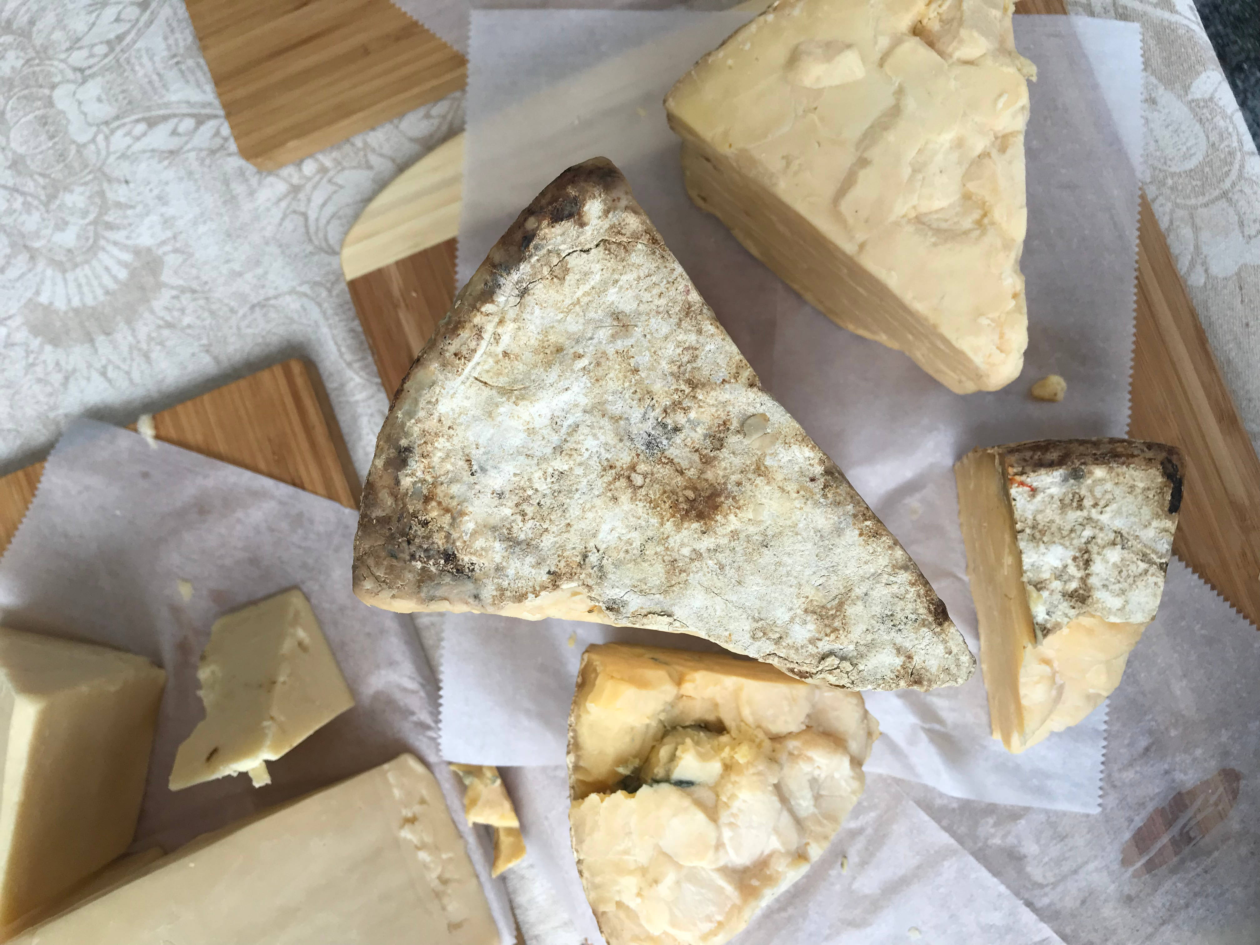 Cheese 桌布 壁紙 — 一個鄉村風格的各式起司擺盤，帶有紋理的外皮和奶油般的內餡，放在烘焙紙上，置於木板上。