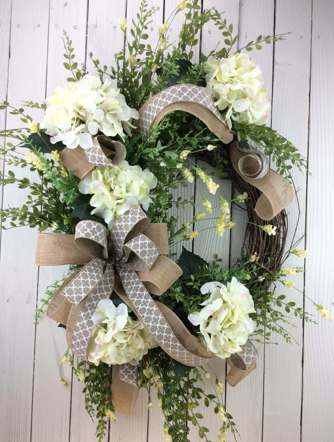 Spring Wreaths 桌布 壁紙 — 一個鄉村風格的春季花環，帶有奶油色繡球花、綠色植物和圖案麻布絲帶，掛在風化的白色木板上。