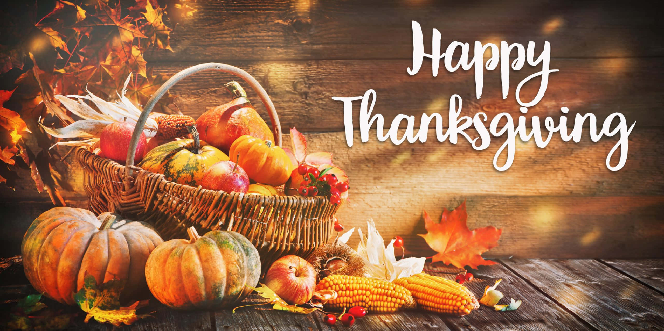 Fall Thanksgiving 桌布 壁紙 — 一個鄉村風格的柳條籃子，裝滿了南瓜、蘋果和玉米，放在木桌上，周圍環繞著秋葉和發光的燈光，並帶有「Happy Thanksgiving」文字。