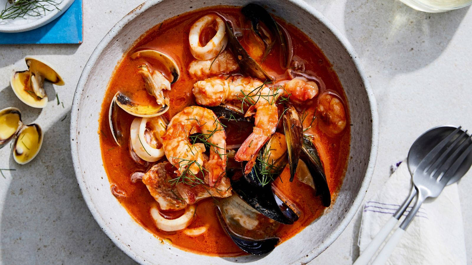 Food Photography 桌布 壁紙 — 一個鄉村風格的海鮮燉湯碗，內有蝦、蛤蜊和魷魚，點綴蒔蘿，放在明亮的檯面上。