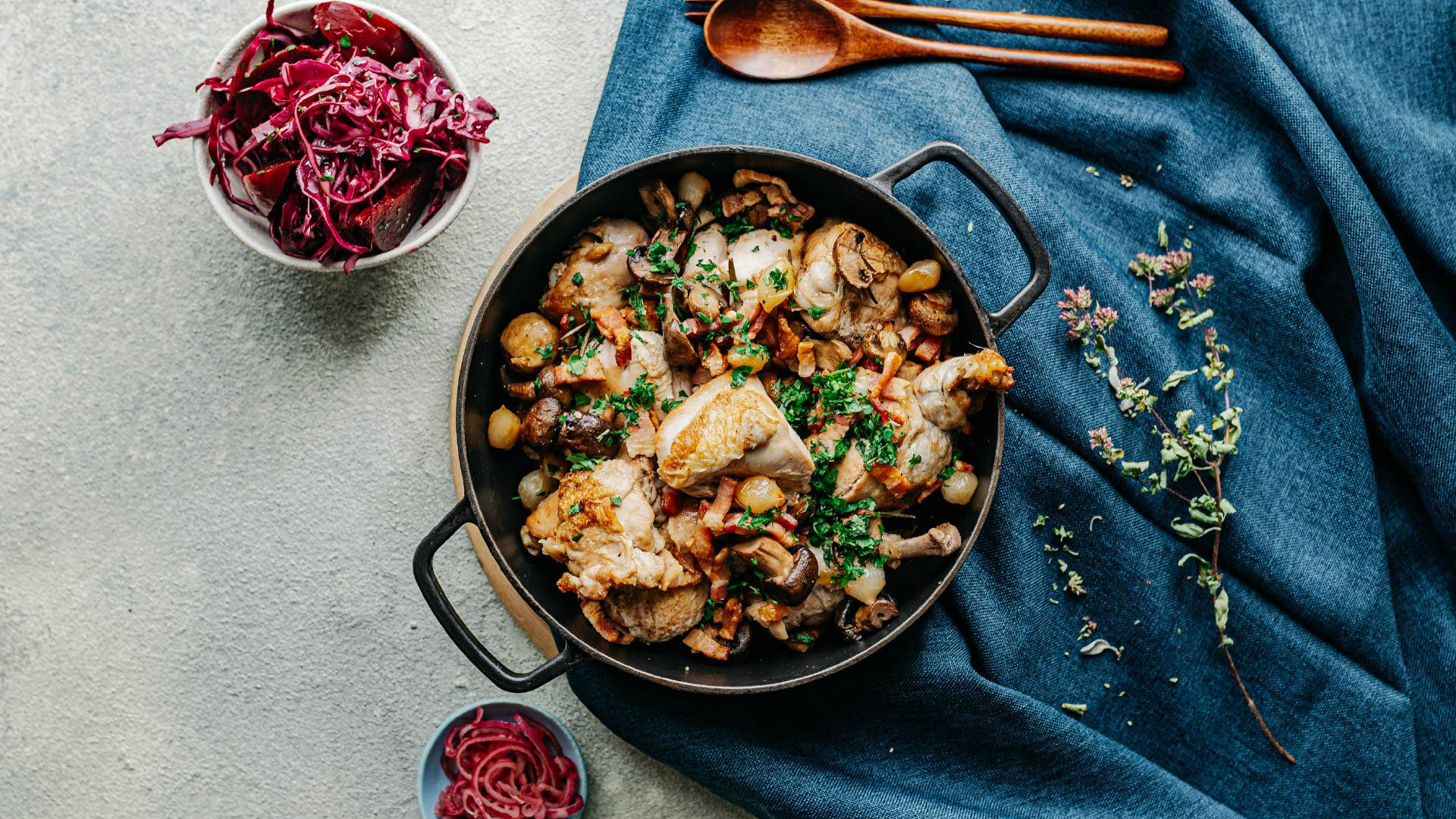 Food Photography 桌布 壁紙 — 一個鄉村風格的煎鍋，裡面有雞肉和蘑菇，上面裝飾著歐芹，旁邊放著紅椰菜碗和木勺，放在藍色布上。