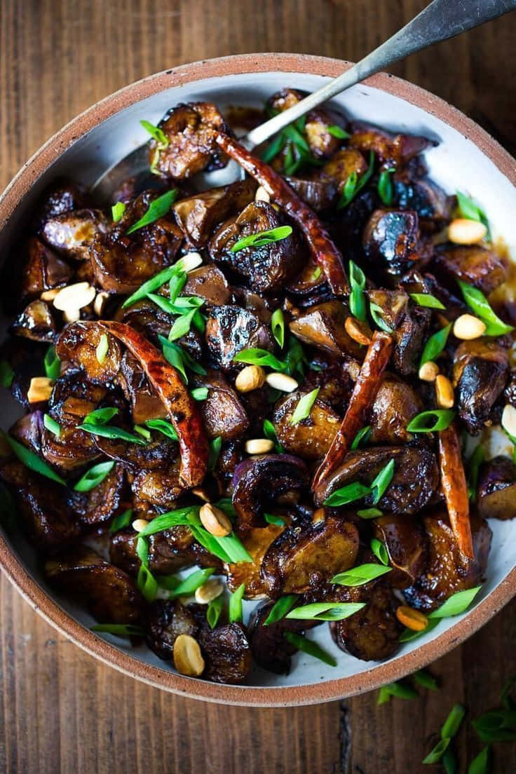 Black Garlic 桌布 壁紙 — 一個鄉村風格的碗，盛載著光澤的烤茄子，配以松子仁和辣椒，並以青蔥點綴。