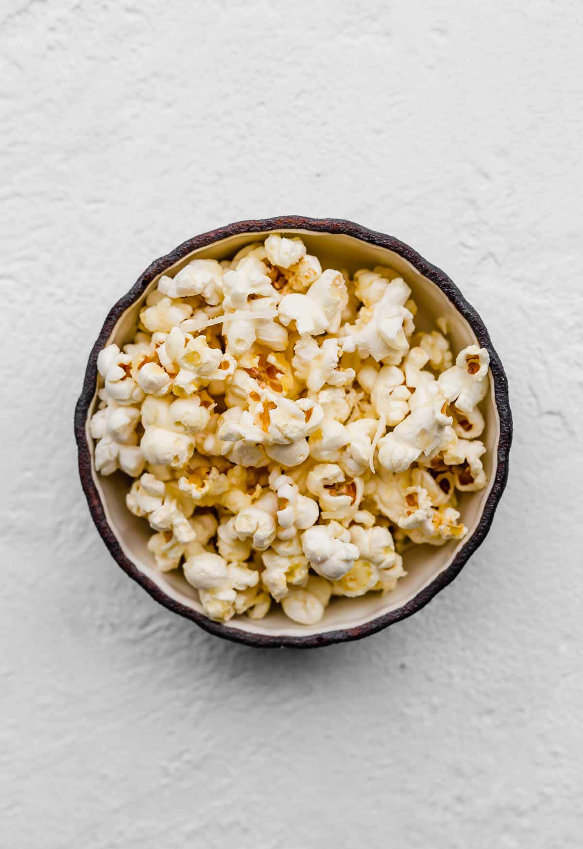 Popcorn 桌布 壁紙 — 一個鄉村風格的碗，裝滿了奶油焦糖爆米花，放在有紋理的白色背景上，俯視圖。