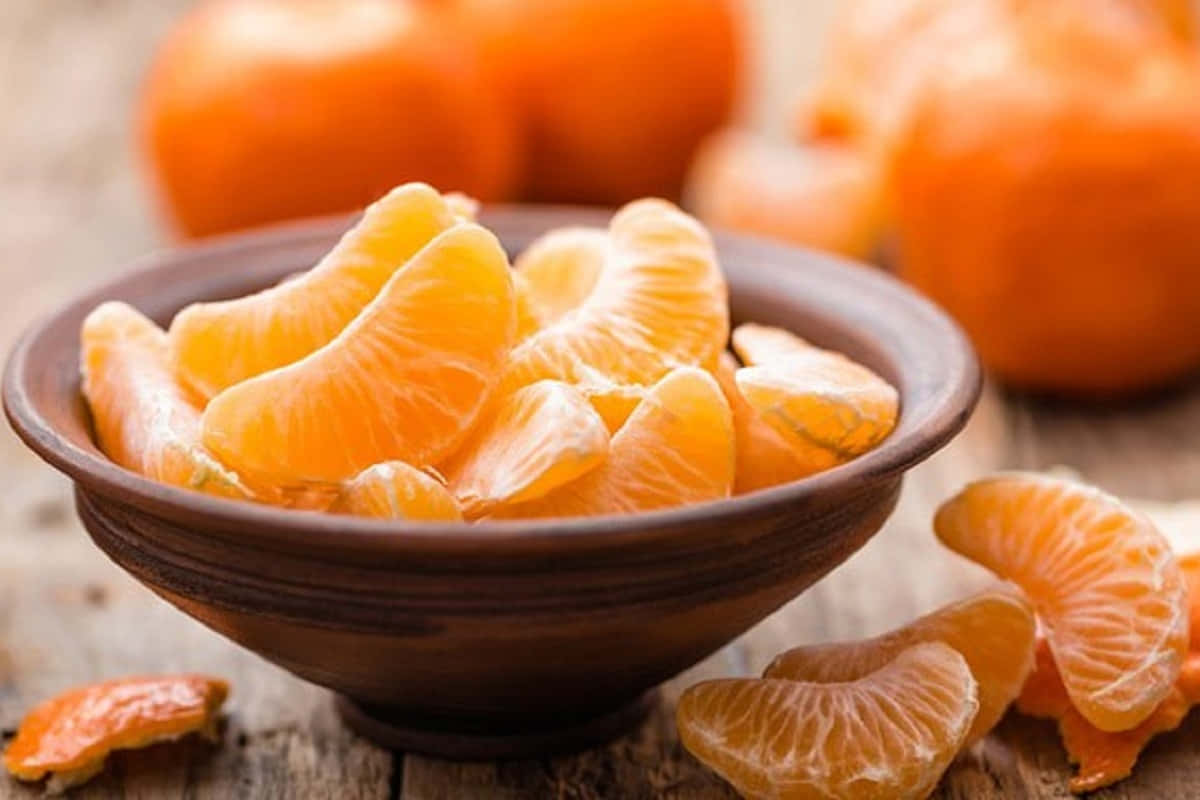 Winter Fruits 桌布 壁紙 — 一個鄉村風格的碗盛滿多汁的柑橘瓣，放在一張風化的木桌上，背景有模糊的完整柑橘。