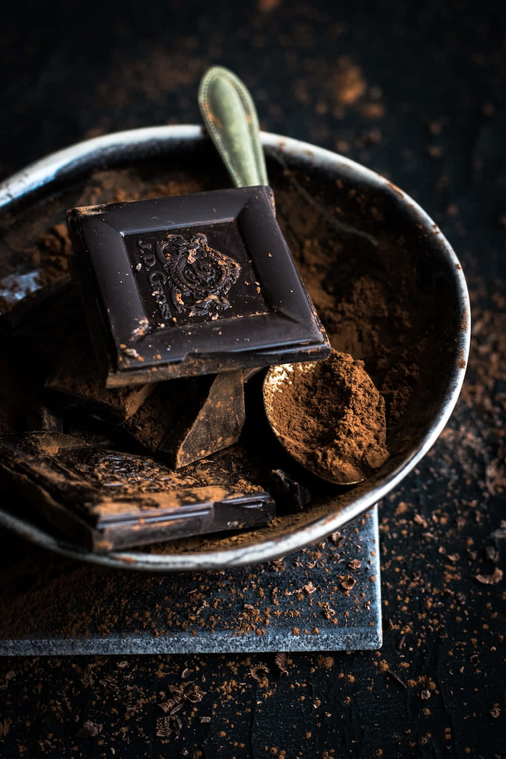 Dark Chocolate 桌布 壁紙 — 一個鄉村風格的碗裡盛著濃郁的黑巧克力條和可可粉，配上一把復古湯匙，背景是深色紋理。