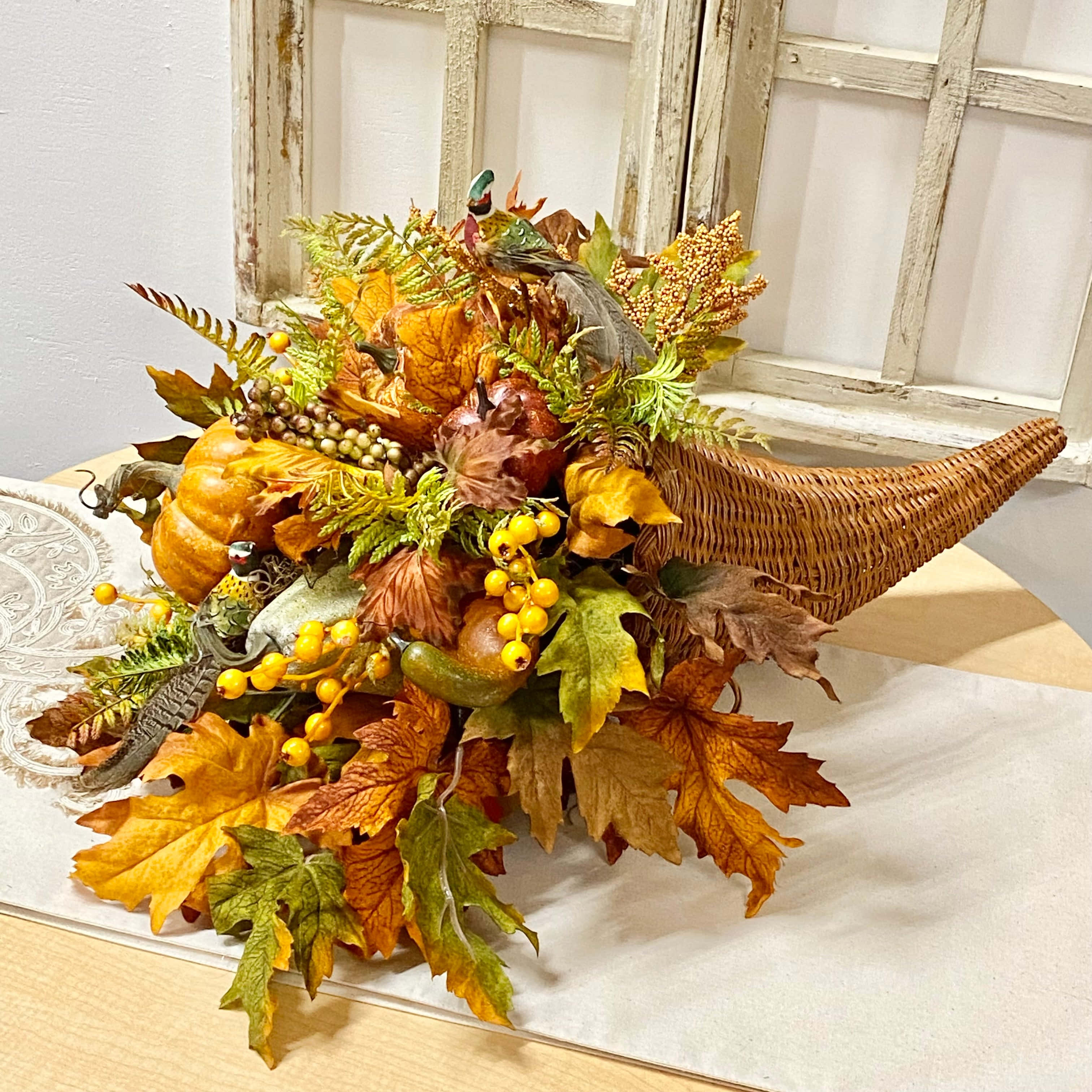 Fall Cornucopia 桌布 壁紙 — 一個鄉村風格的秋季豐收角，裝滿了南瓜、漿果和鮮豔的秋葉，放在靠近風化窗戶的蕾絲桌布上。