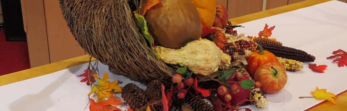 Fall Cornucopia 桌布 壁紙 — 一個鄉村風格的秋季豐收角，裝滿了南瓜、葫蘆、玉米和彩色樹葉，放在白色桌子上。