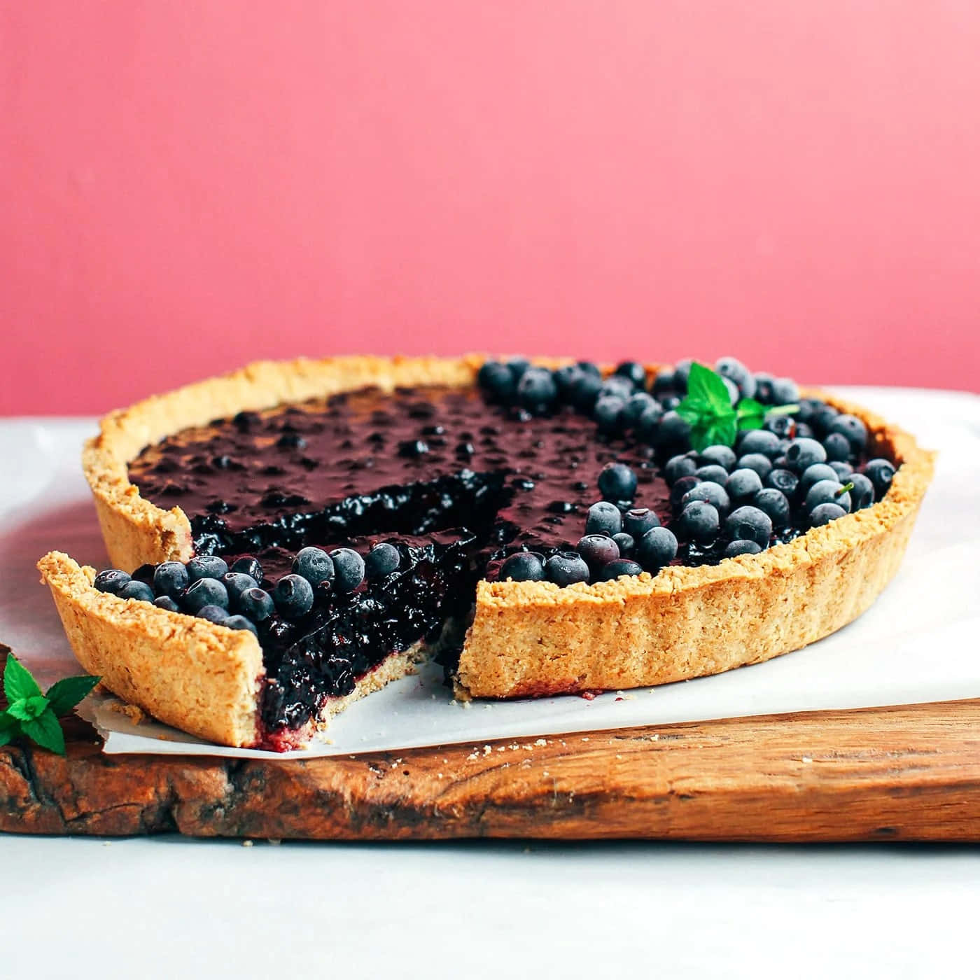 Blueberries Tart 桌布 壁紙 — 一個鄉村風格的藍莓塔，金黃色的外皮放在木板上，切開一片露出多汁的餡料和新鮮薄荷裝飾。