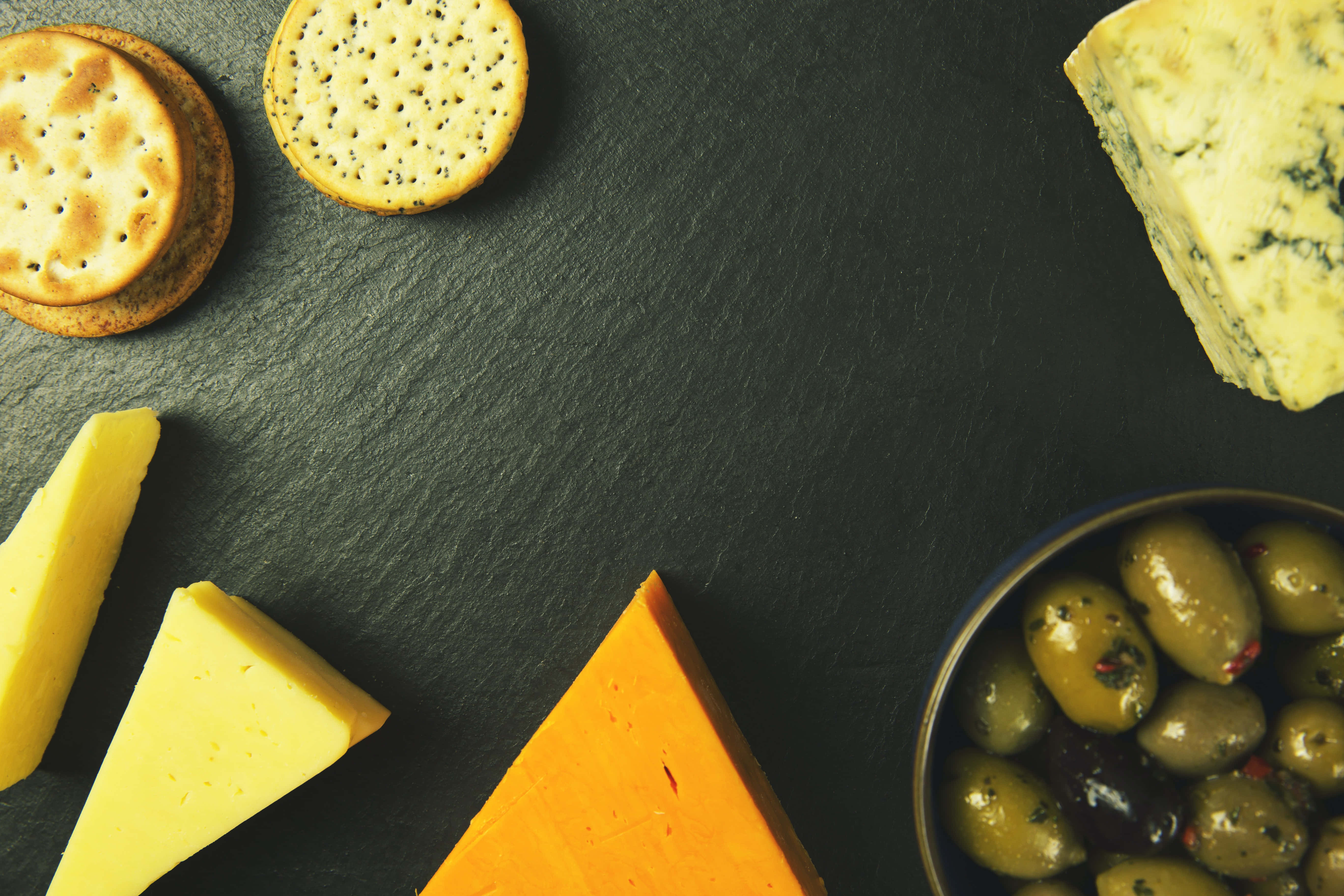 Cheese 桌布 壁紙 — 一個鄉村風格的起司拼盤，上面擺放著各種起司、餅乾和橄欖，置於深色石板表面上。