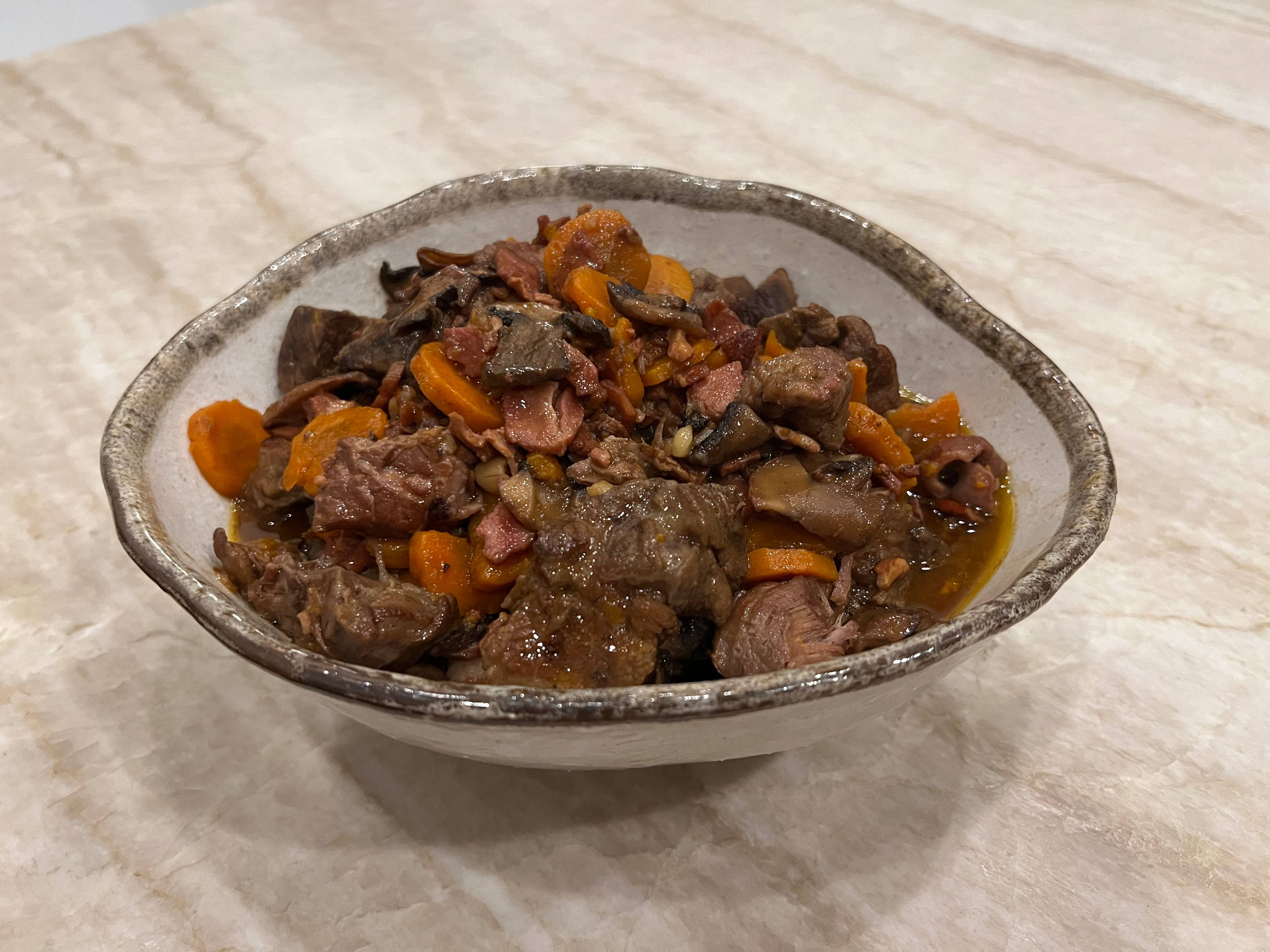 meat 桌布 壁紙 — 一個鄉村風格的陶瓷碗，裡面裝滿了濃郁的燉肉和紅蘿蔔，放在大理石檯面上。