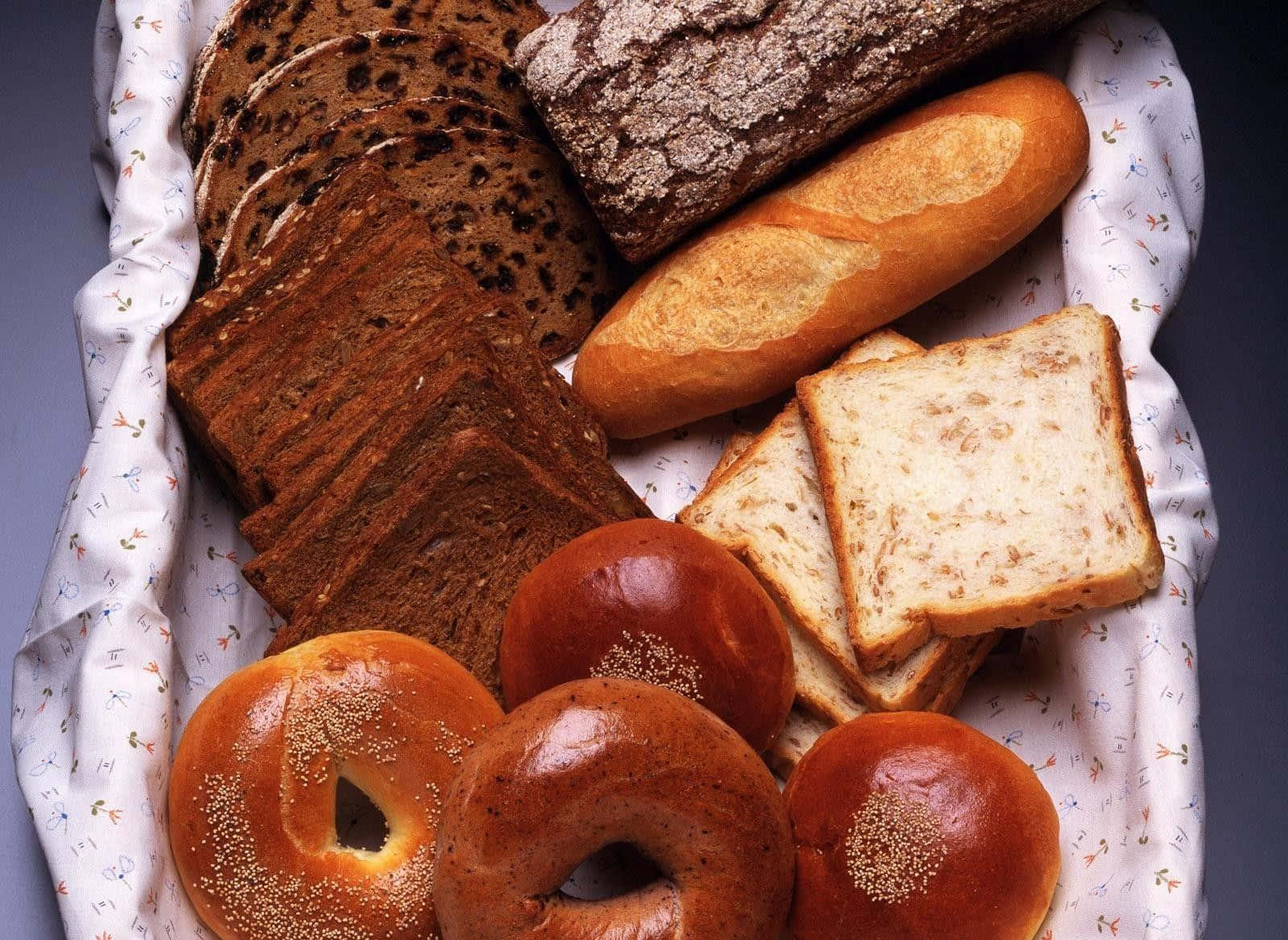 Bakery 桌布 壁紙 — 一個鄉村風格籃子，裝滿各種新鮮麵包，包括百吉餅、黑麥麵包和酸種麵包片。
