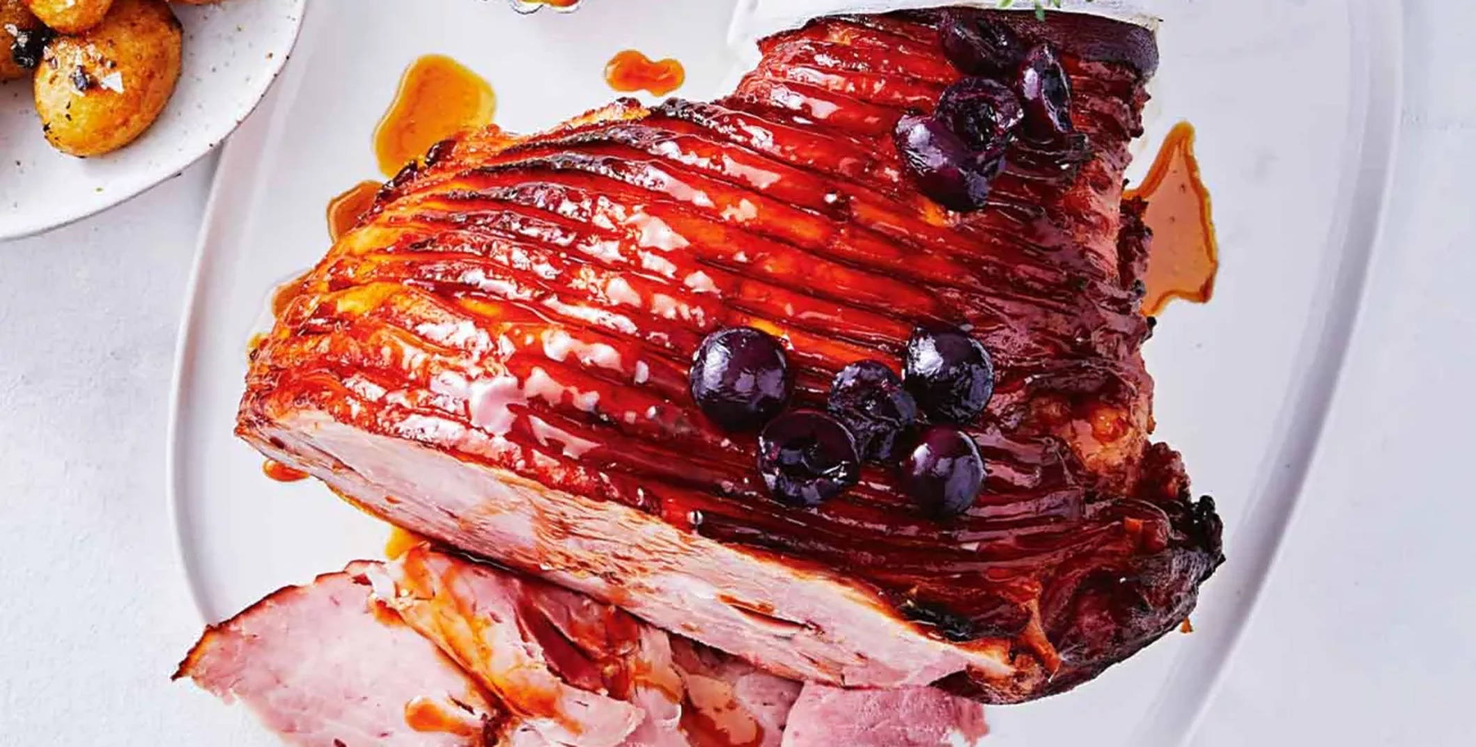 Ham 桌布 壁紙 — 一個釉面烤火腿配櫻桃和醬汁，切片放在白色托盤上，旁邊有烤馬鈴薯。