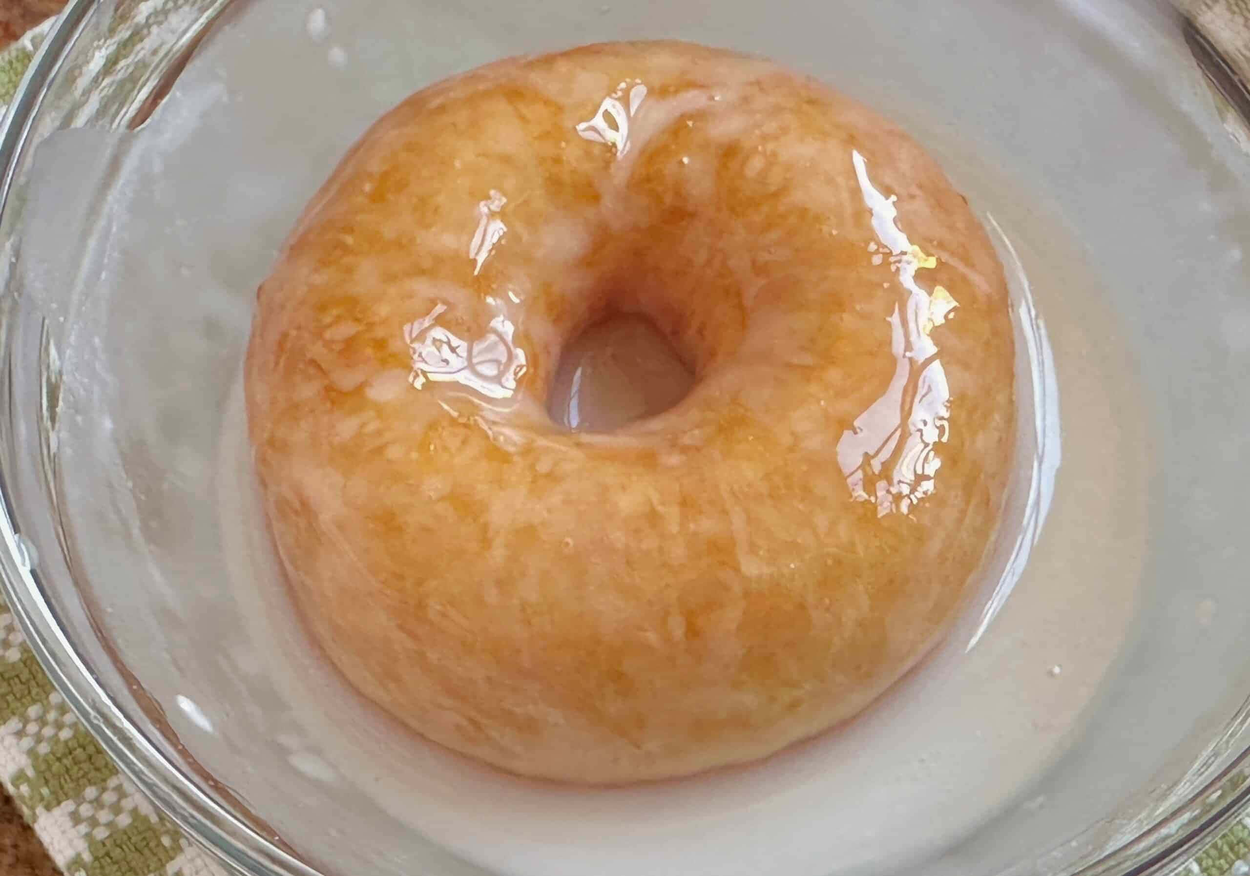 Glazed Donut 桌布 壁紙 — 一個釉面甜甜圈放在透明玻璃碗中，帶有光澤的糖衣反射光線。