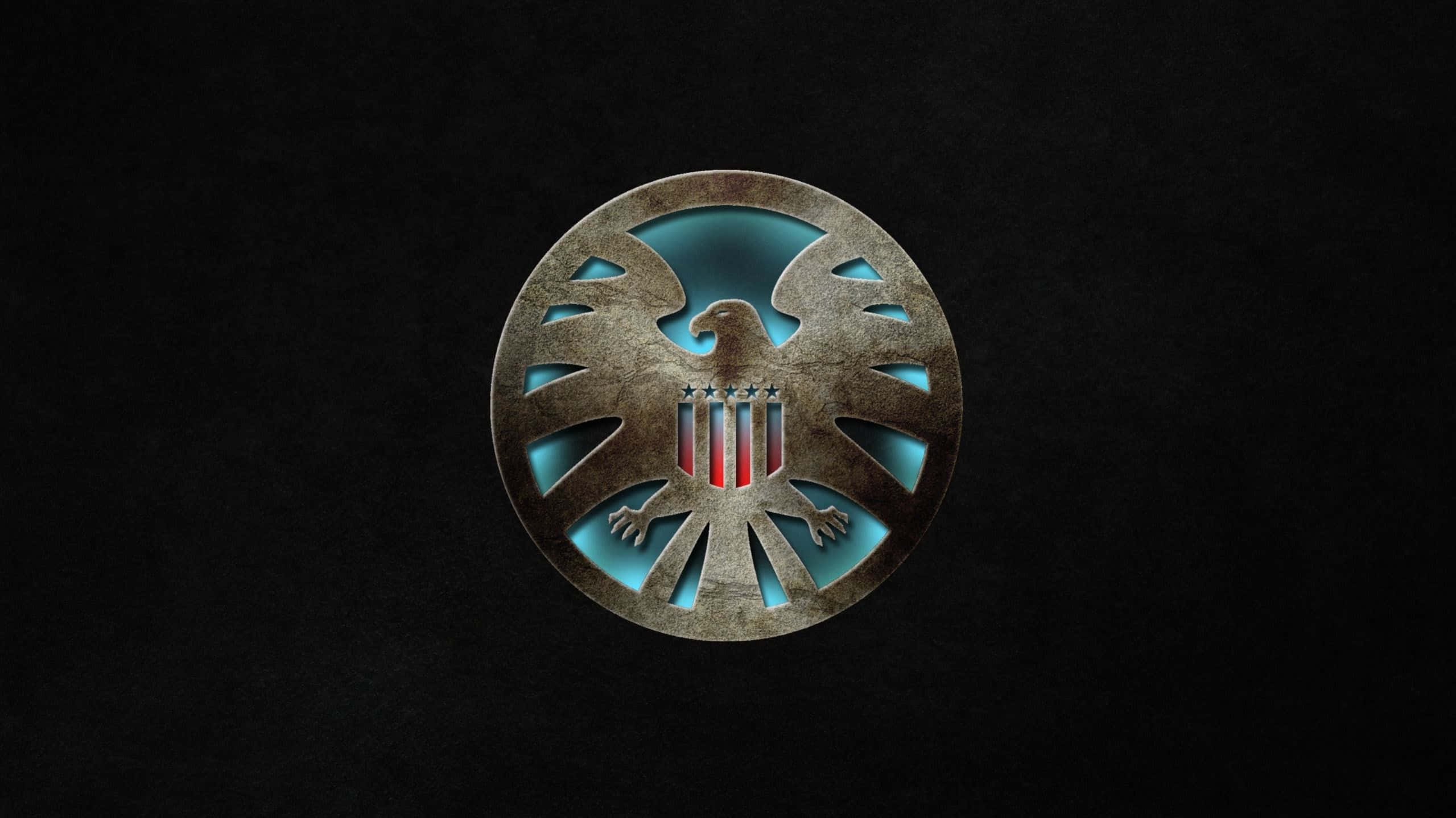 shield 桌布 壁紙 — 一個金屬圓形徽章，上面有一隻發光的藍色老鷹，抓著紅白條紋的橫條，背景是黑色紋理。