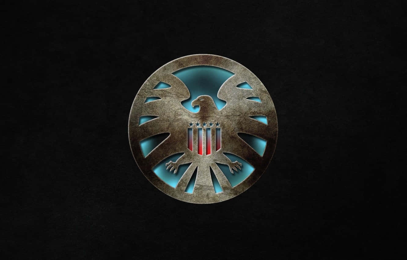 Marvel Logo 桌布 壁紙 — 一個金屬圓形徽章，上面有鷹和盾牌，在深色紋理背景上發出藍色和紅色的光芒。