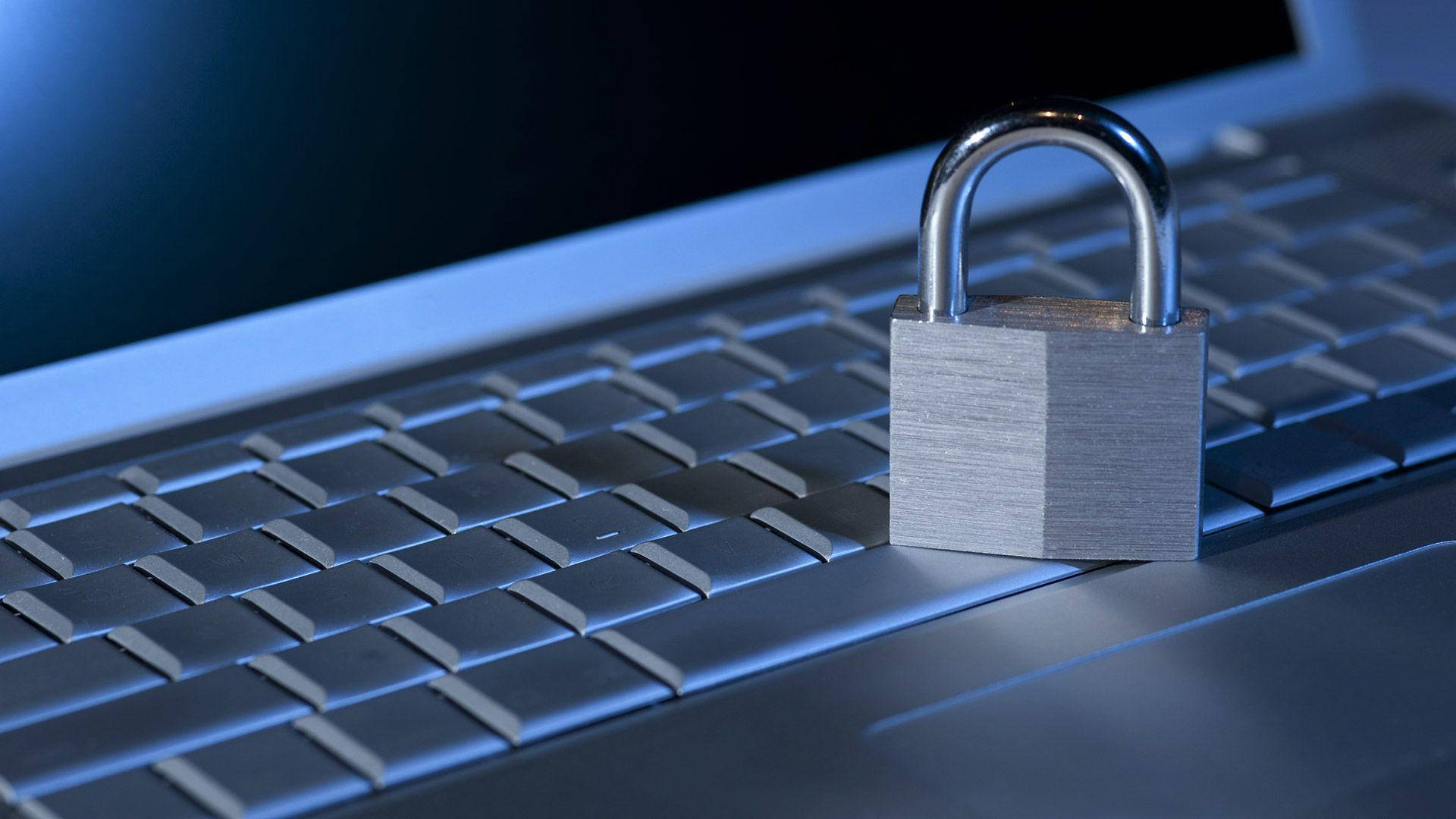 security 桌布 壁紙 — 一個金屬掛鎖放在筆記型電腦鍵盤上，在冷藍色燈光下強調數位安全。