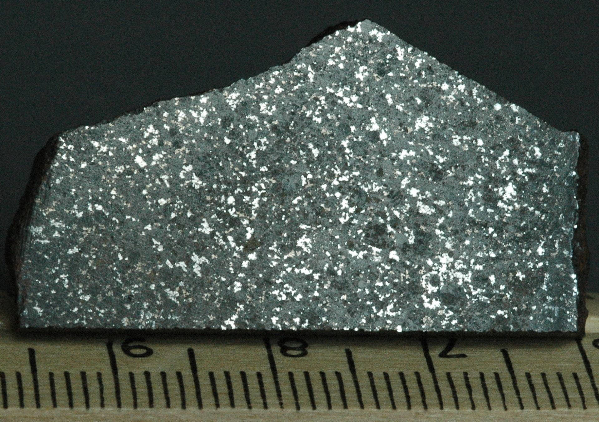 Material 桌布 壁紙 — 一個金屬灰色岩石的特寫，帶有閃爍的銀色斑點，放在木尺上，背景為深色。