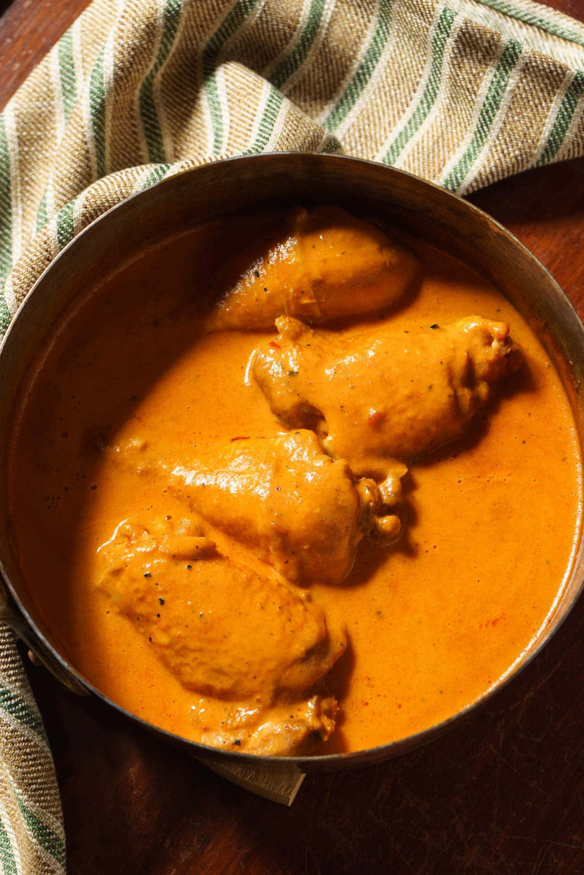 Chicken 桌布 壁紙 — 一個金屬碗盛載著濃郁的橙色雞肉咖哩，放在木桌的條紋布上慢煮。