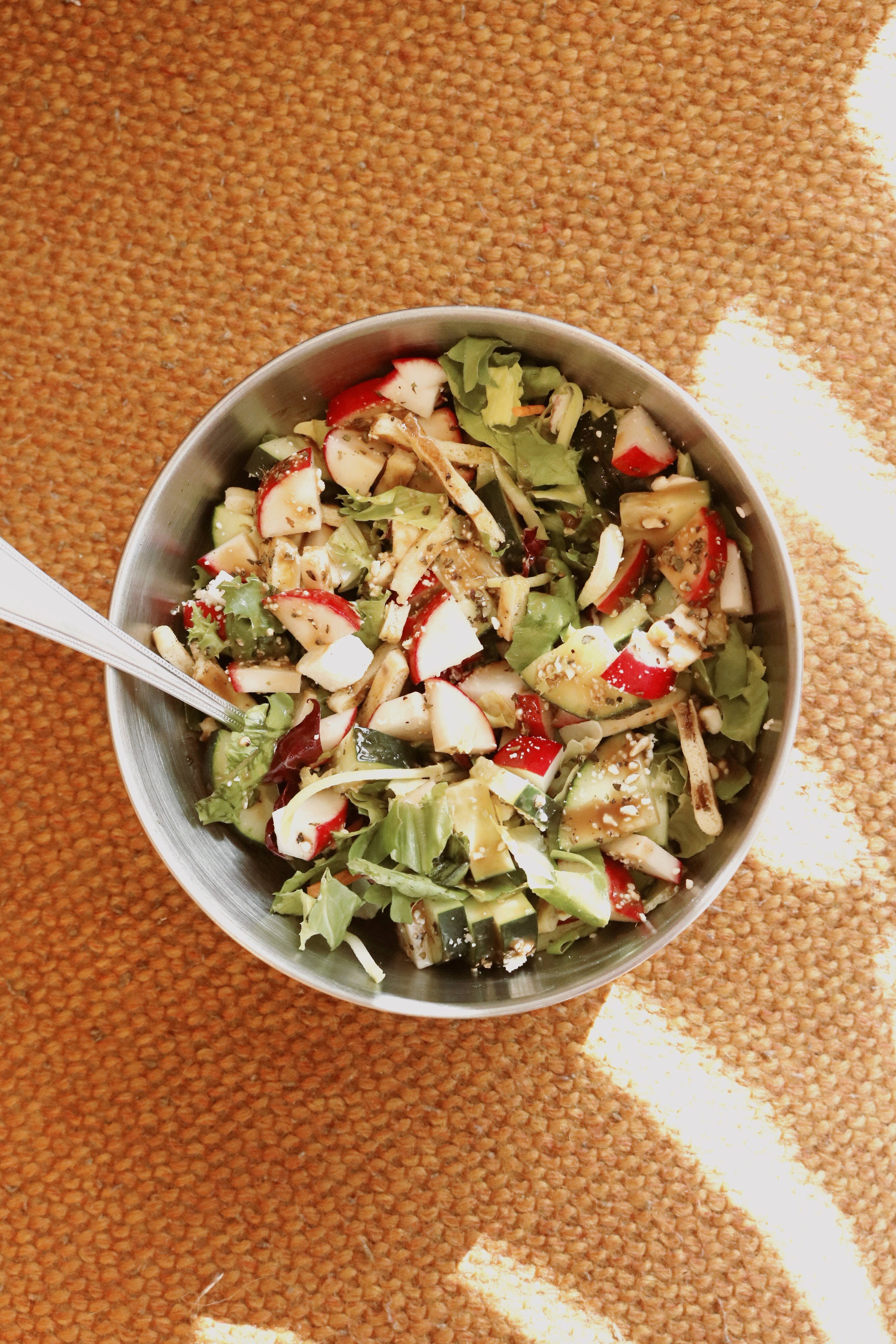 Salad 桌布 壁紙 — 一個金屬碗裡裝著新鮮的沙拉，有蘿蔔、小黃瓜和蔬菜，放在有紋理的橙色表面上。