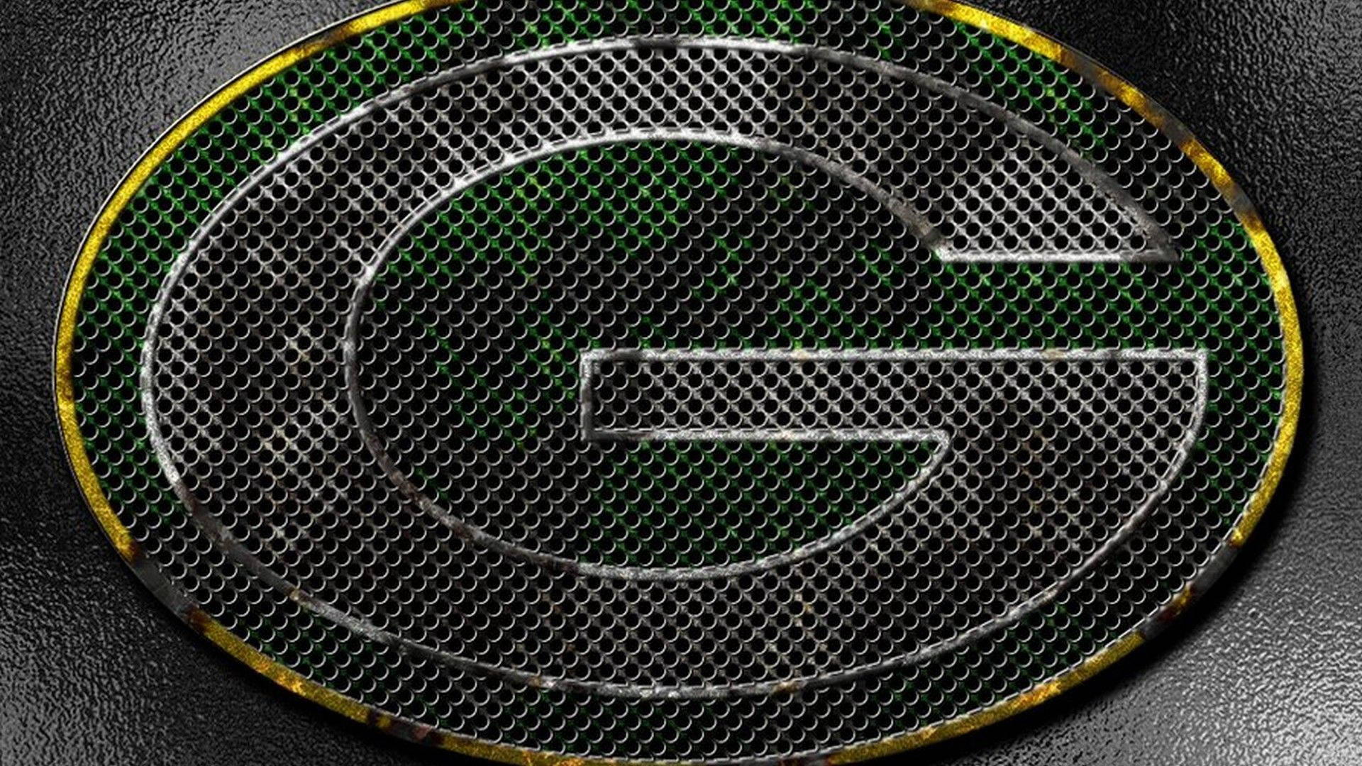 Packers 桌布 壁紙 — 一個金屬綠色的 'G' 標誌蝕刻在穿孔金屬格柵上，帶有風化的金色邊框，背景是深色紋理。