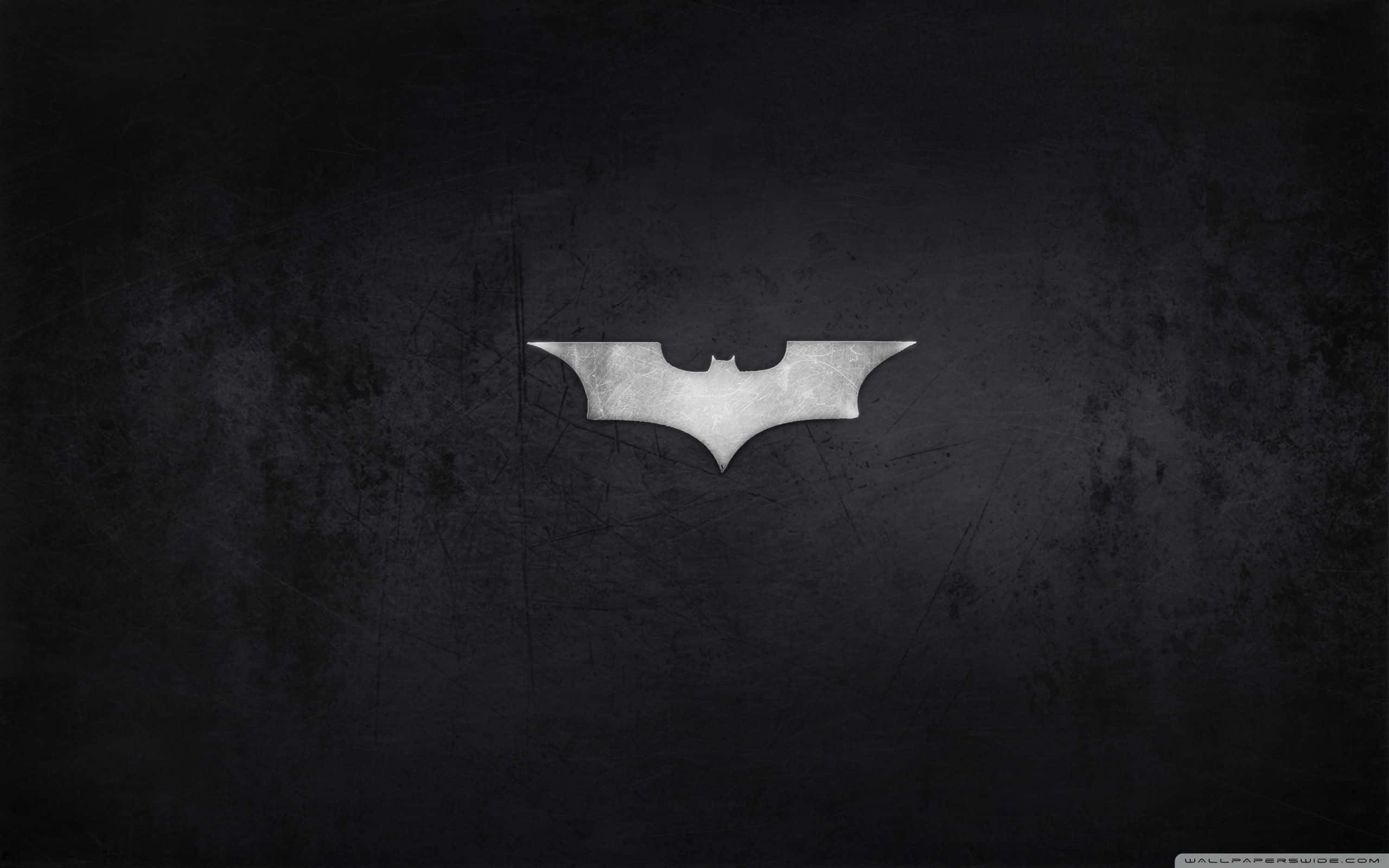 Batmobile Desktop 桌布 壁紙 — 一個金屬蝙蝠標誌在帶有刮痕和污垢的深色紋理牆壁上隱約發光。