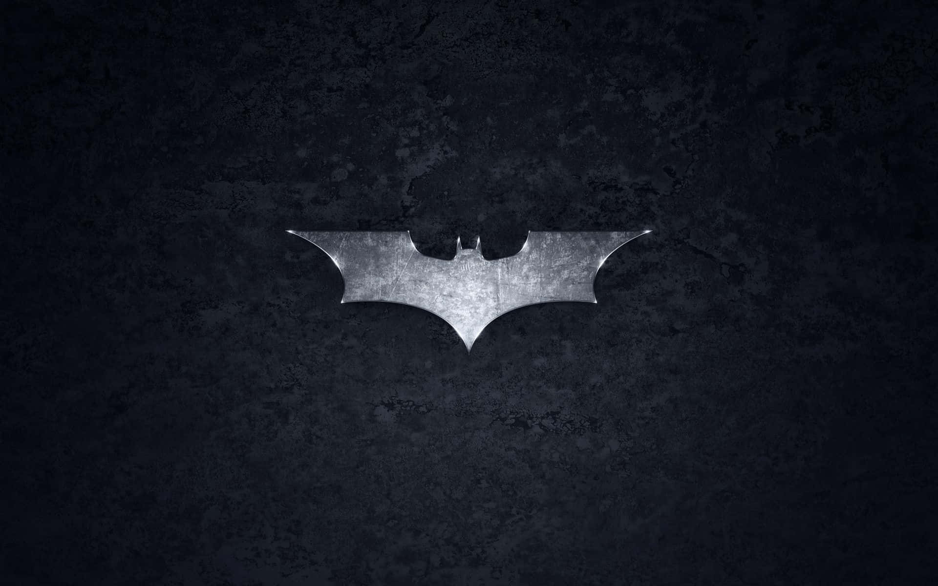 Batmobile Desktop 桌布 壁紙 — 一個金屬蝙蝠標誌在聚光燈下，映襯粗糙的深色混凝土牆壁閃耀。