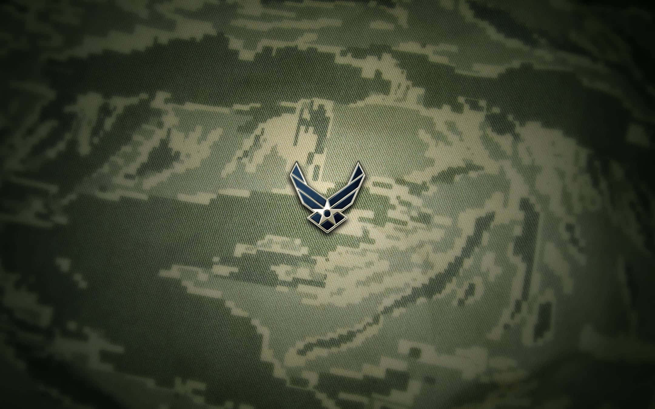Air Force 桌布 壁紙 — 一個金屬製的美國空軍翼章在數位迷彩布料背景中央閃耀。