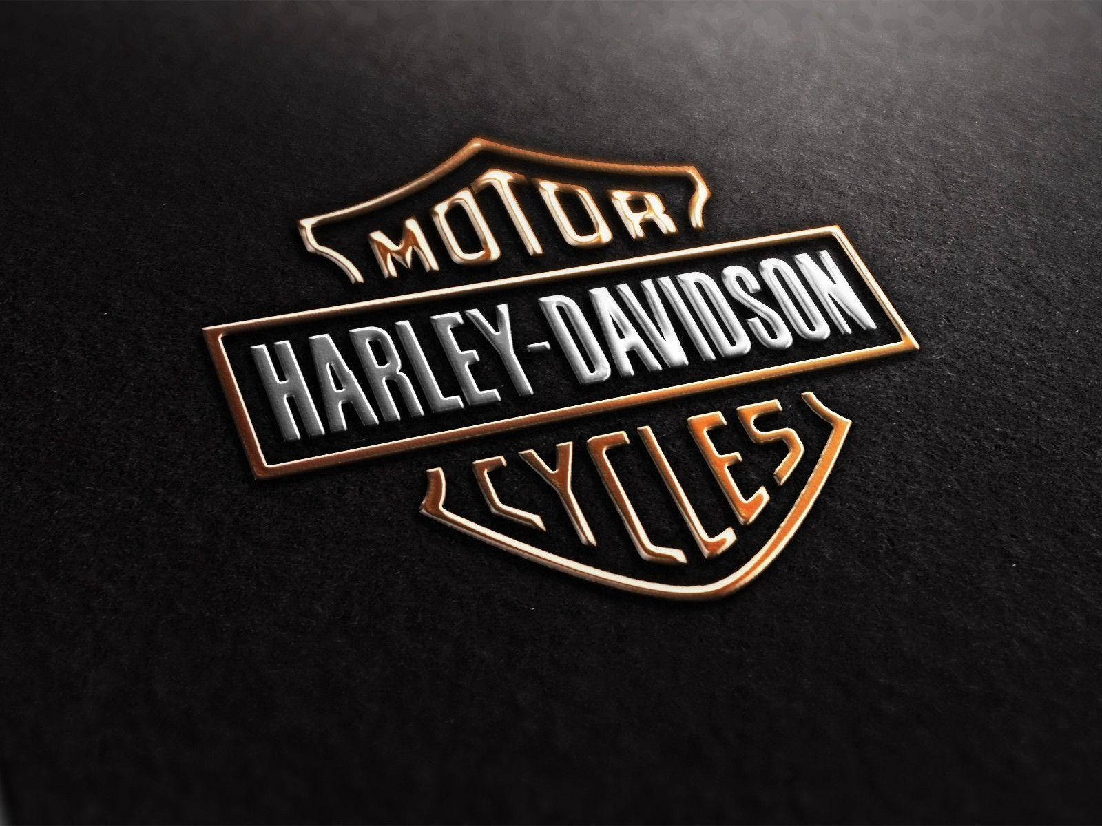Harley 桌布 壁紙 — 一個金屬質感的Harley-Davidson標誌徽章，在帶有紋理的黑色背景上閃耀著金色和銀色的點綴。