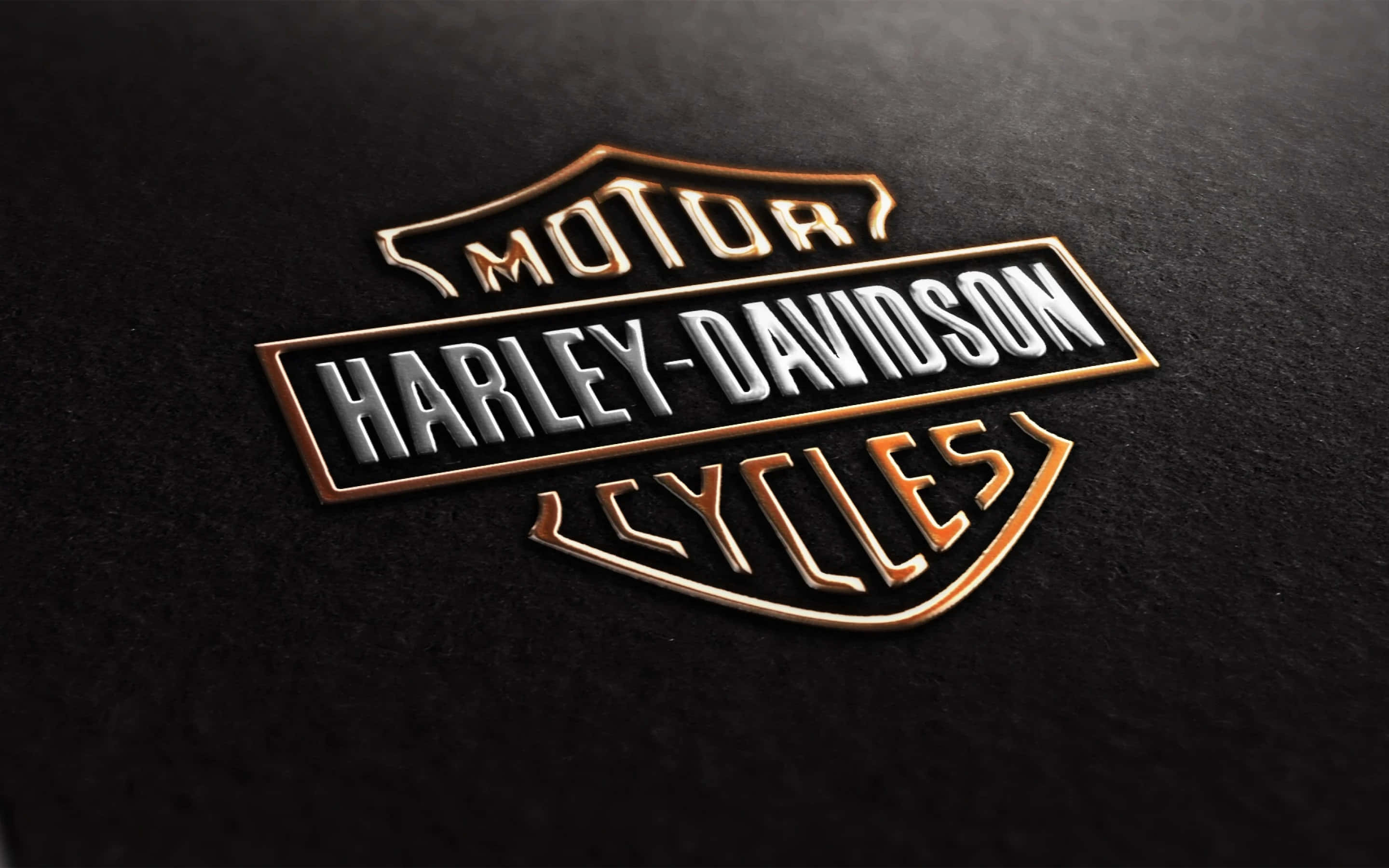 Harley Davidson Motorcycle Free 桌布 壁紙 — 一個金屬質感的Harley-Davidson標誌徽章，在紋理黑色背景上閃耀著金色和銀色點綴。