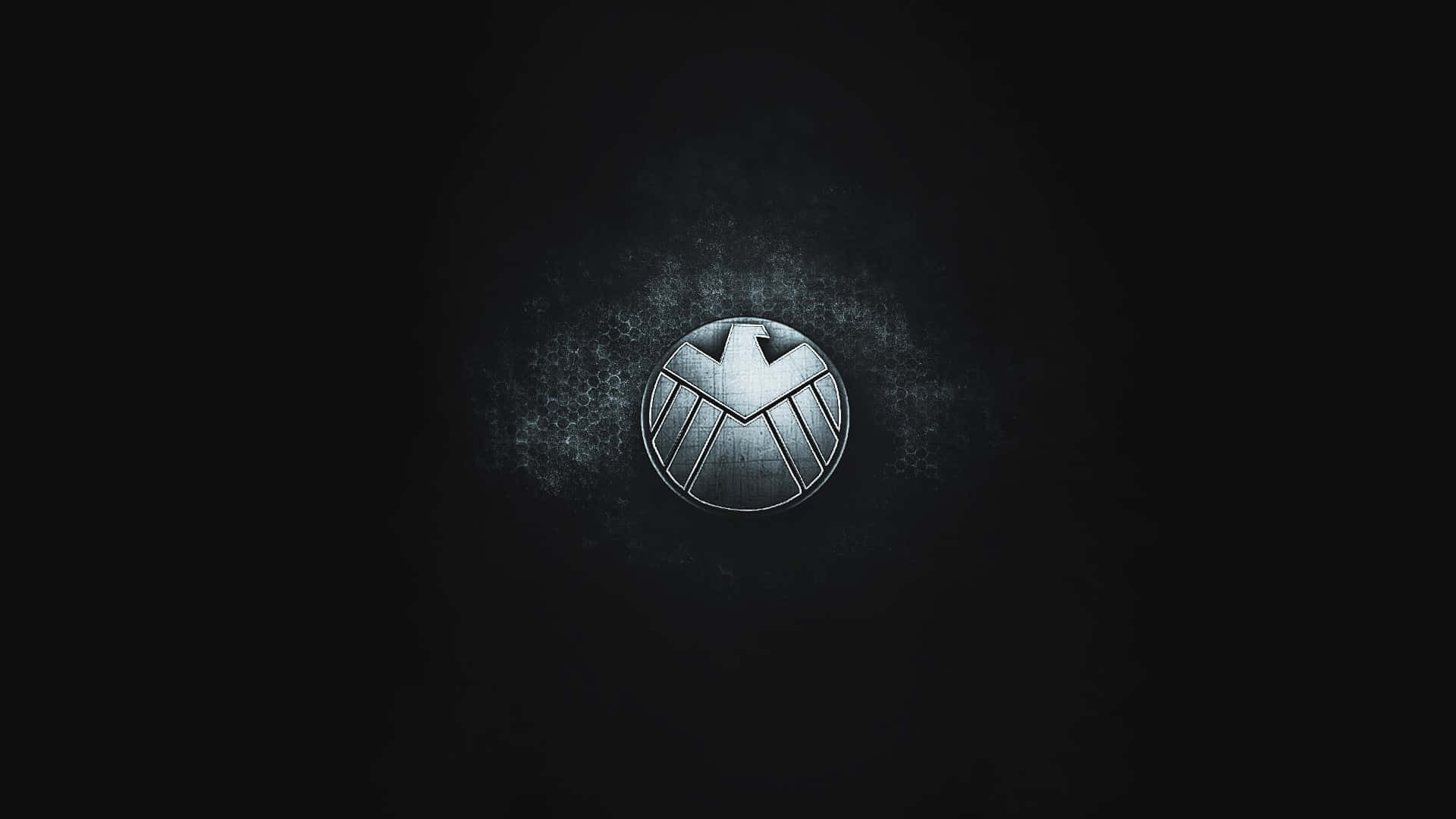 shield 桌布 壁紙 — 一個金屬質感的S.H.I.E.L.D.標誌在深色紋理背景上隱約發光，背後有微妙的光線散發出來。