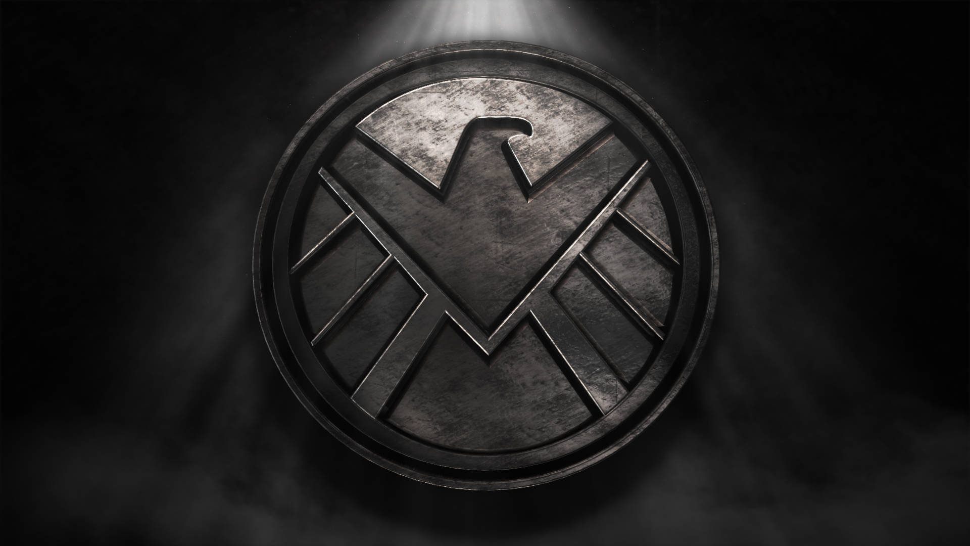 Marvel Logo 桌布 壁紙 — 一個金屬質感的SHIELD標誌在聚光燈下發光，背景是煙霧瀰漫的黑暗環境。
