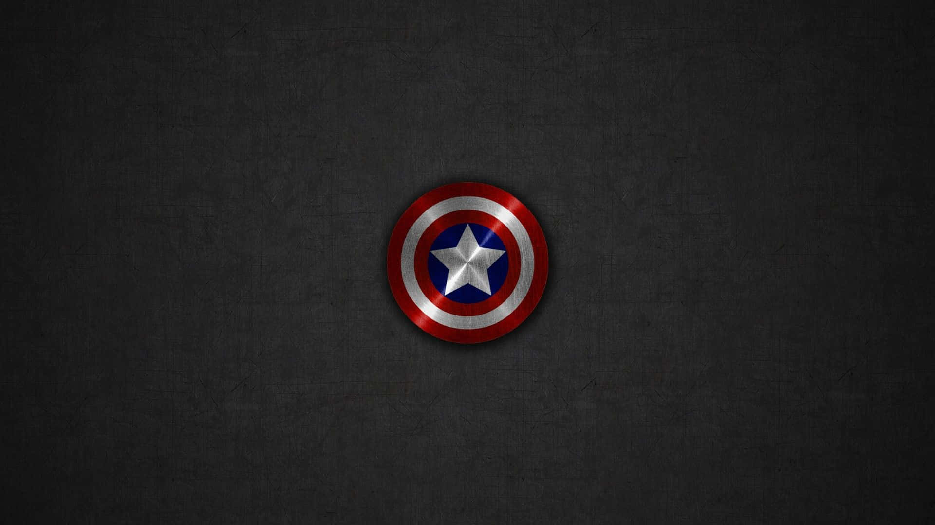 Captain America Logo 桌布 壁紙 — 一個金屬質感的美國隊長盾牌，居中放置在帶有細微照明的紋理深灰色背景上。