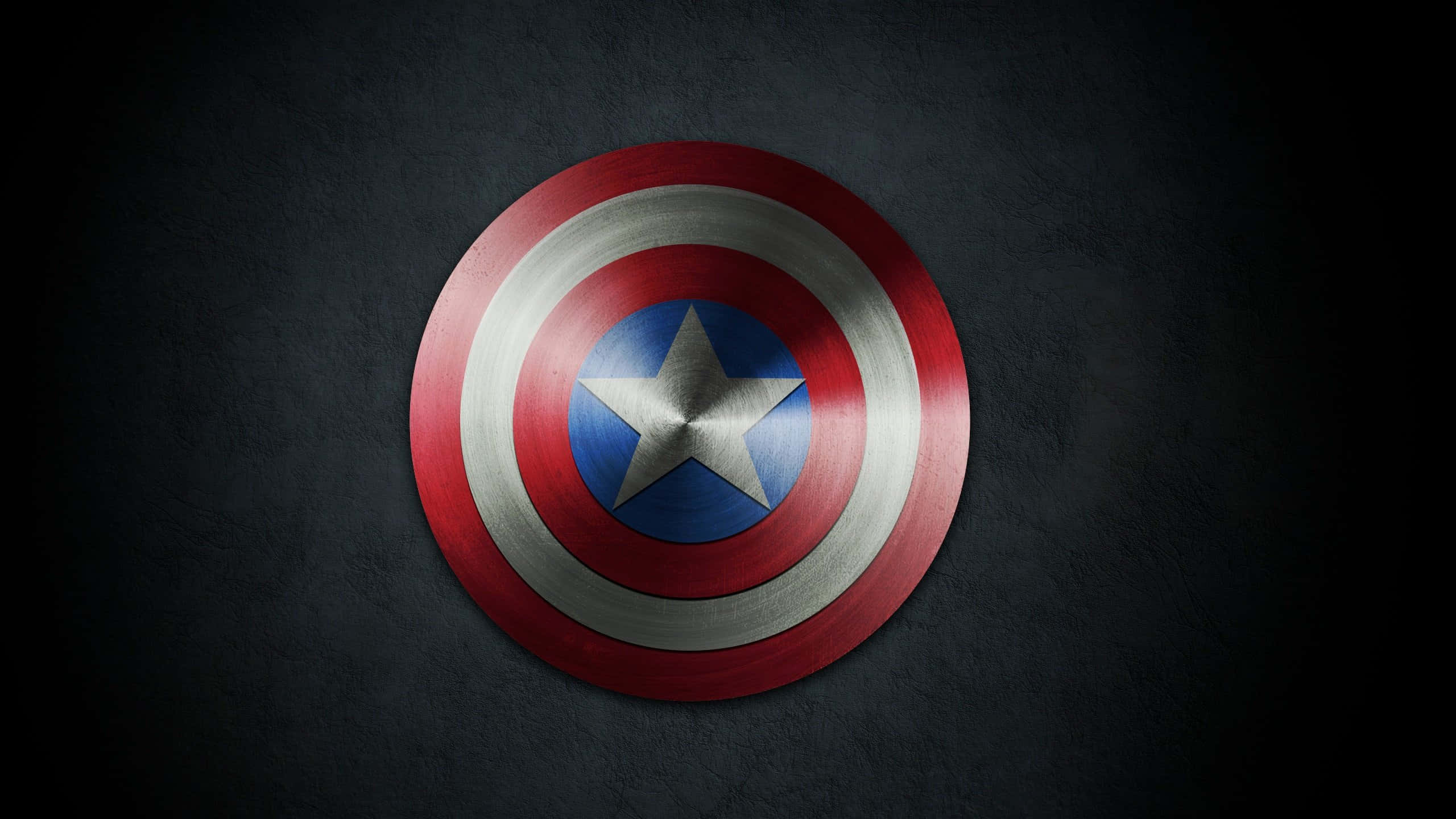 Marvel Aesthetic 桌布 壁紙 — 一個金屬質感的美國隊長盾牌，帶有紅、白、藍同心圓和星星，置於深色紋理牆上。