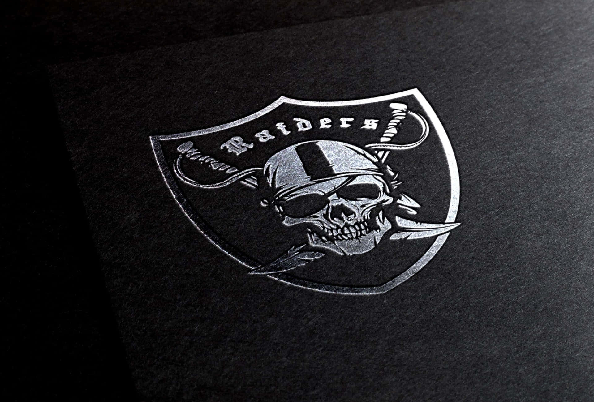 Raiders標誌，在深色紋理背景上有一個骷髏頭和交叉的劍。 — 突襲者 GIF 壁紙