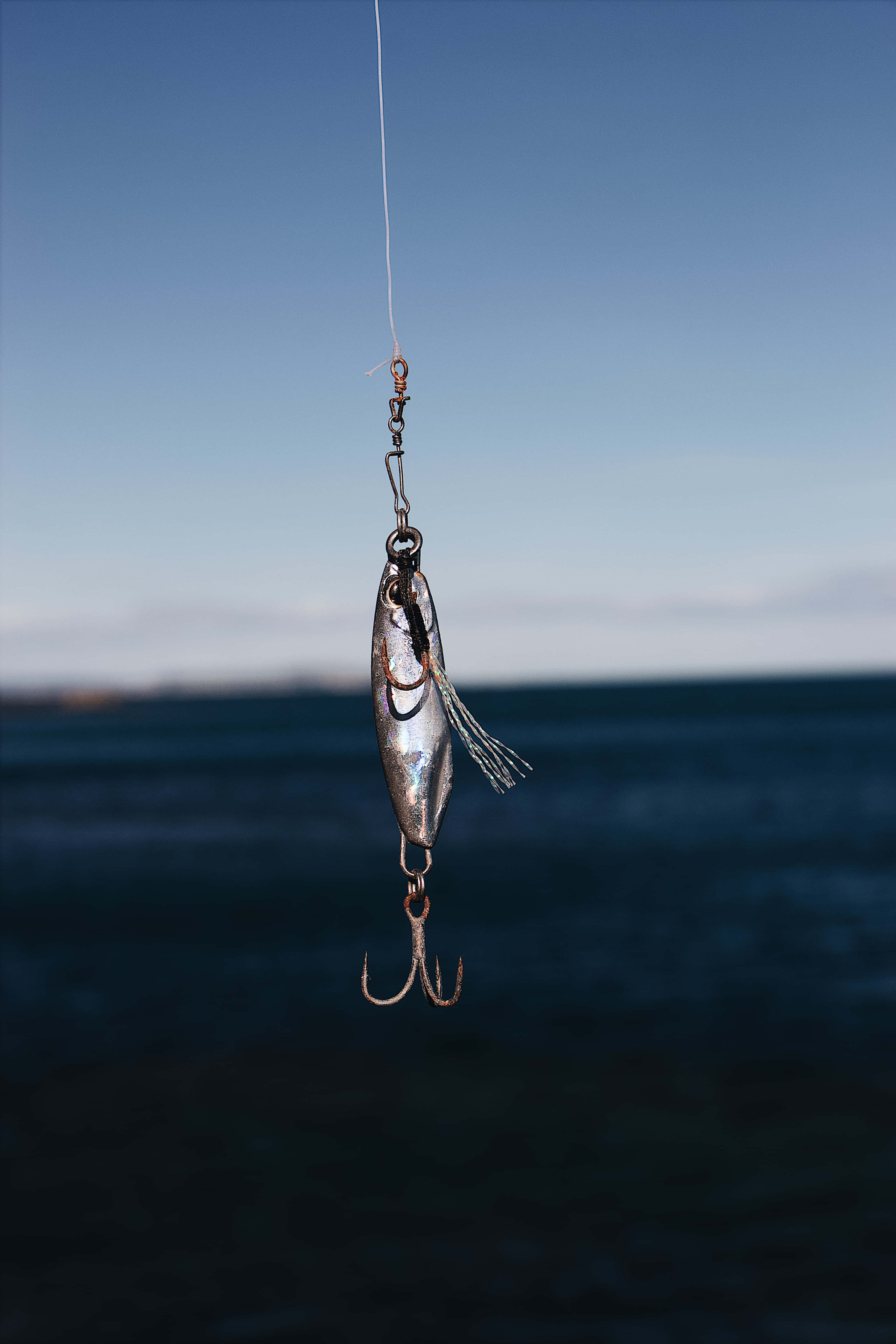 Fishing Rod 桌布 壁紙 — 一個金屬魚餌懸掛在平靜的海洋和清澈的藍天下。