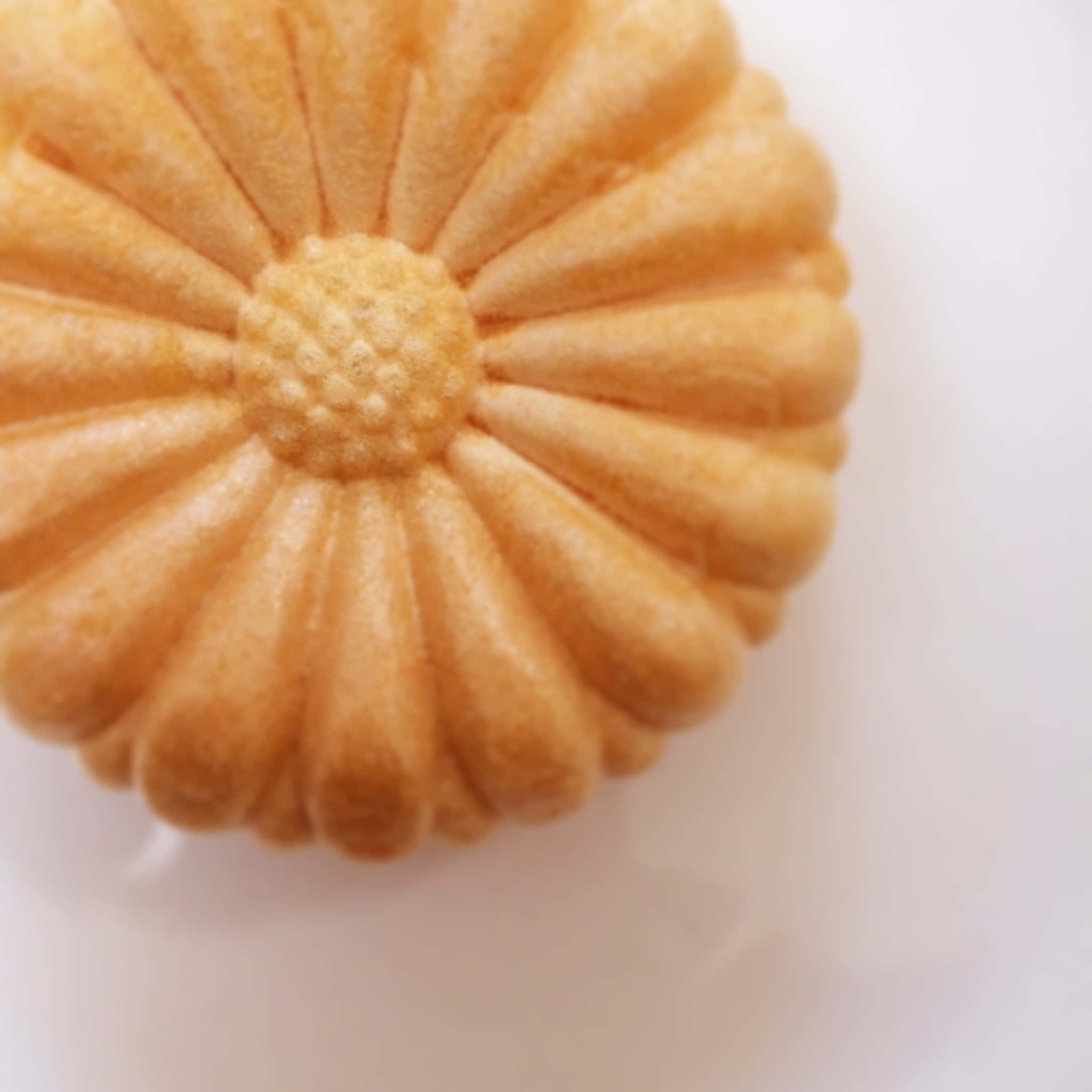 Japanese Sweets 桌布 壁紙 — 一個金棕色花形餅乾的特寫，帶有紋理花瓣，放在純白色表面上。