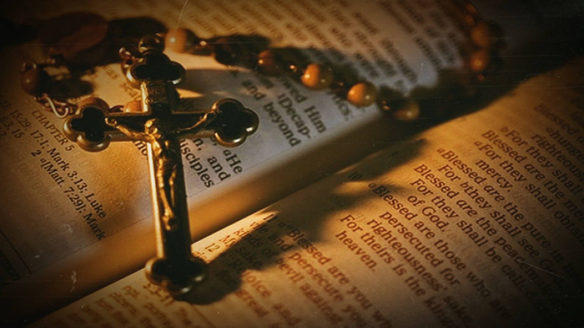 Christ 桌布 壁紙 — 一個金色十字架和玫瑰經念珠放在一本打開的聖經頁面上，沐浴在溫暖的金色光芒中。
