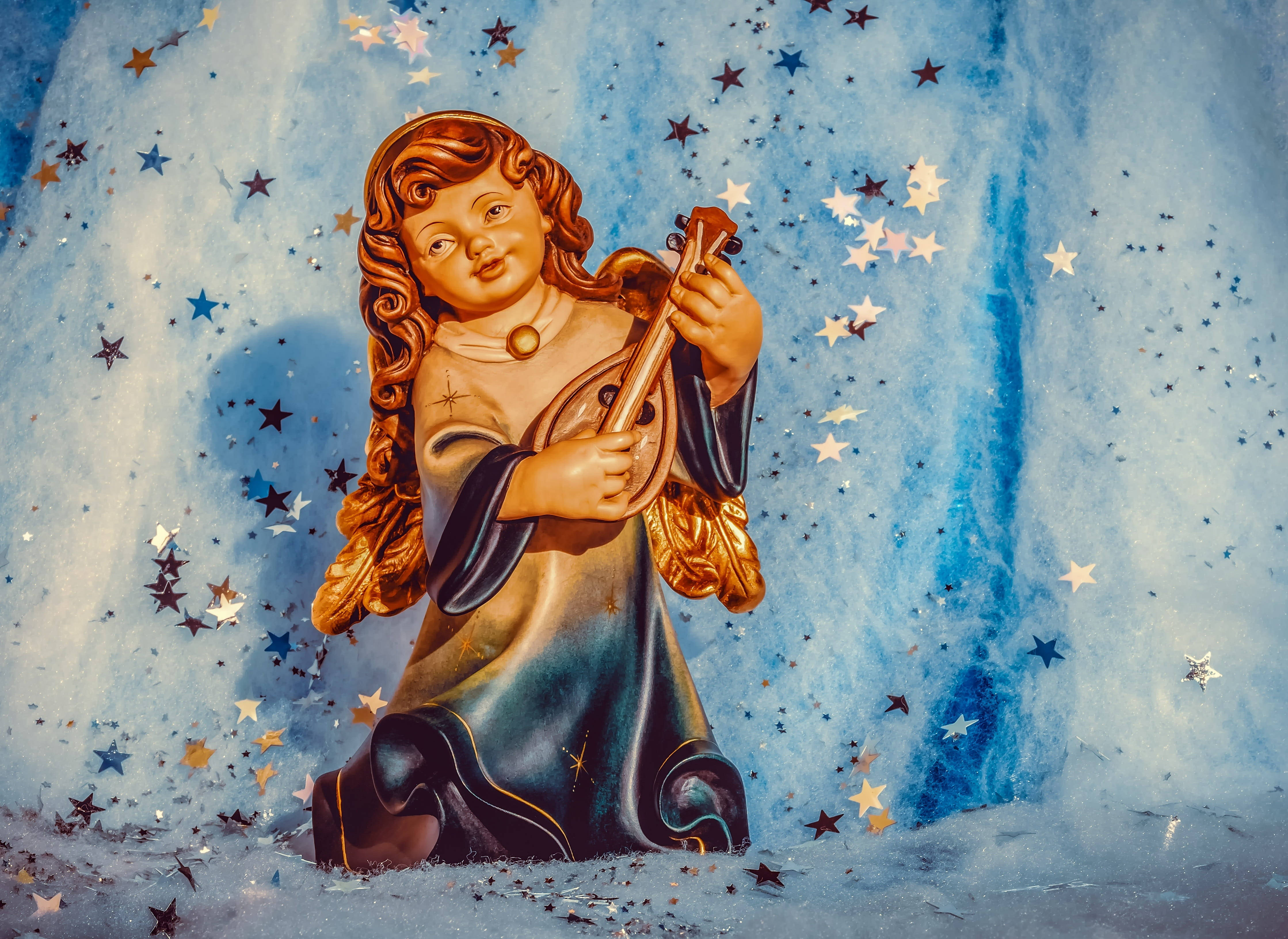 angels 桌布 壁紙 — 一個金色天使雕像跪著，手持琵琶，背景是星光閃爍的藍色夜空，散落著閃爍的星星。