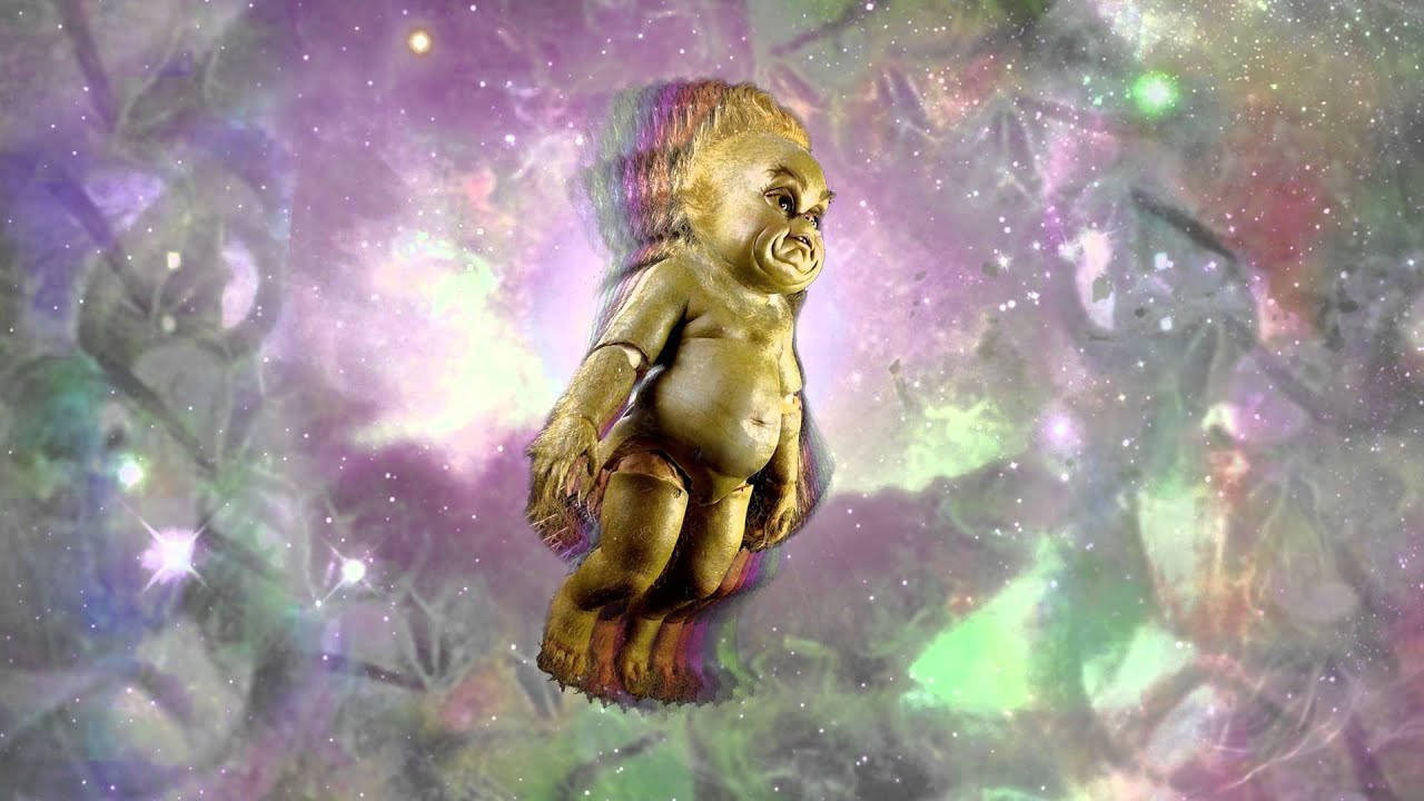 Baby Grinch 桌布 壁紙 — 一個金色嬰兒娃娃漂浮在旋轉的宇宙星雲中，散發著紫色、綠色和白色的星星光芒。