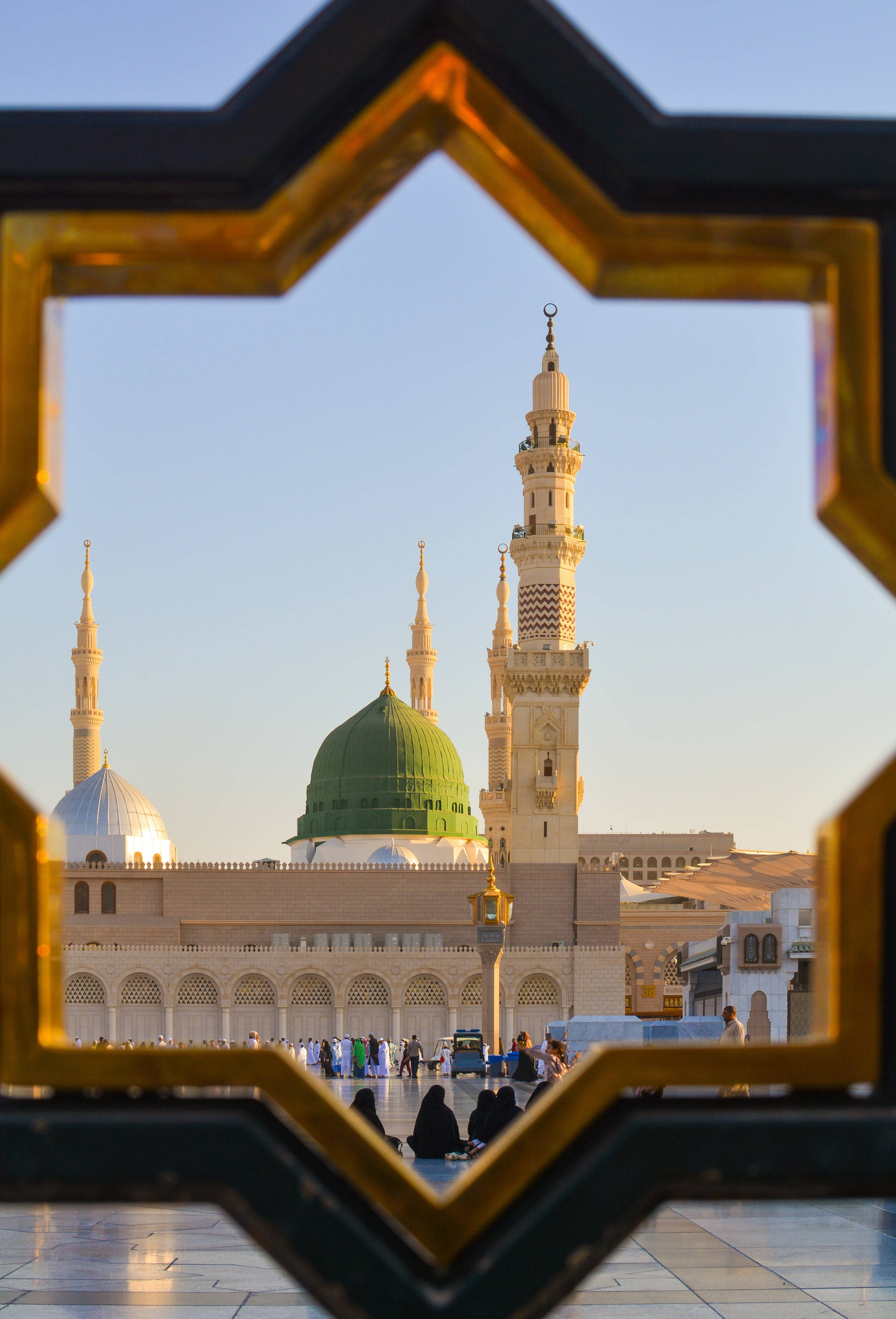 Madina Full HD 桌布 壁紙 — 一個金色星形框架捕捉了宏偉清真寺的綠色圓頂和宣禮塔，背景是清澈的藍天。