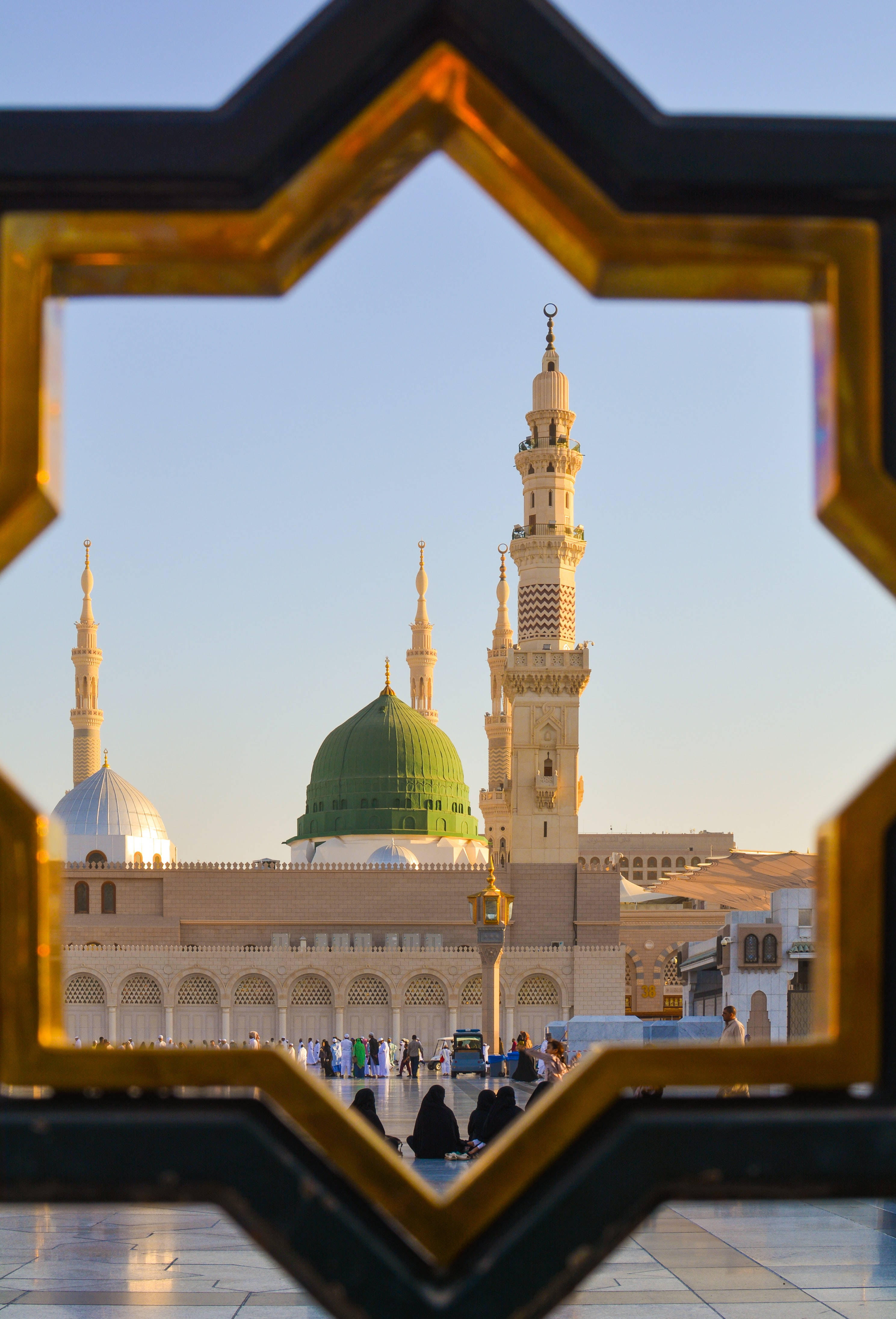 Madina 桌布 壁紙 — 一個金色星形框架捕捉了宏偉清真寺的綠色圓頂和宣禮塔，背景是清澈的藍天。