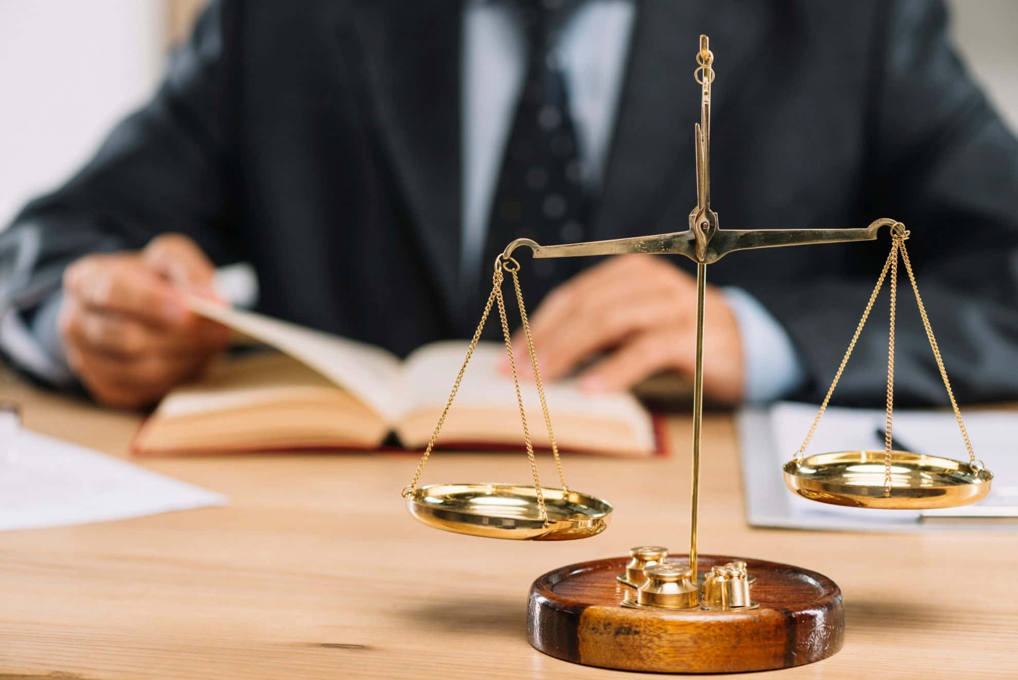 Lawyer 桌布 壁紙 — 一個金色的正義天秤顯眼地放在木桌上，背後有一位穿著西裝的模糊律師正在寫書。