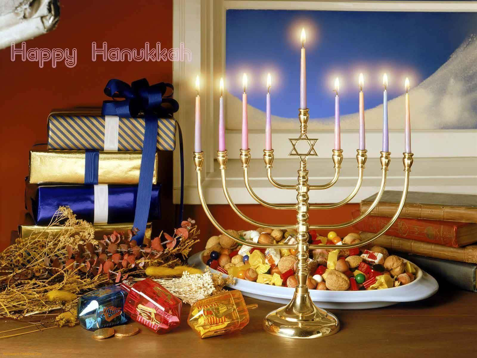 光明節 桌布 壁紙 — 一個金色的燭台（Menorah）上點燃著蠟燭，旁邊放著一盤甜點和包裝好的禮物在木桌上。