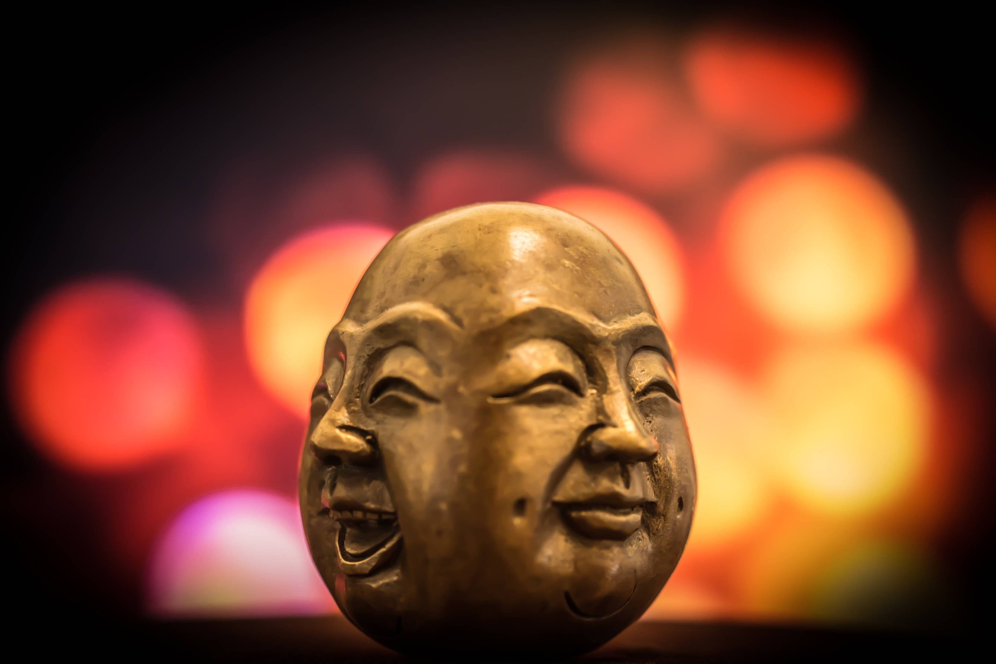 Face 桌布 壁紙 — 一個金色的笑佛頭像雕塑在紅色和橙色燈光的溫暖散景背景下閃耀。