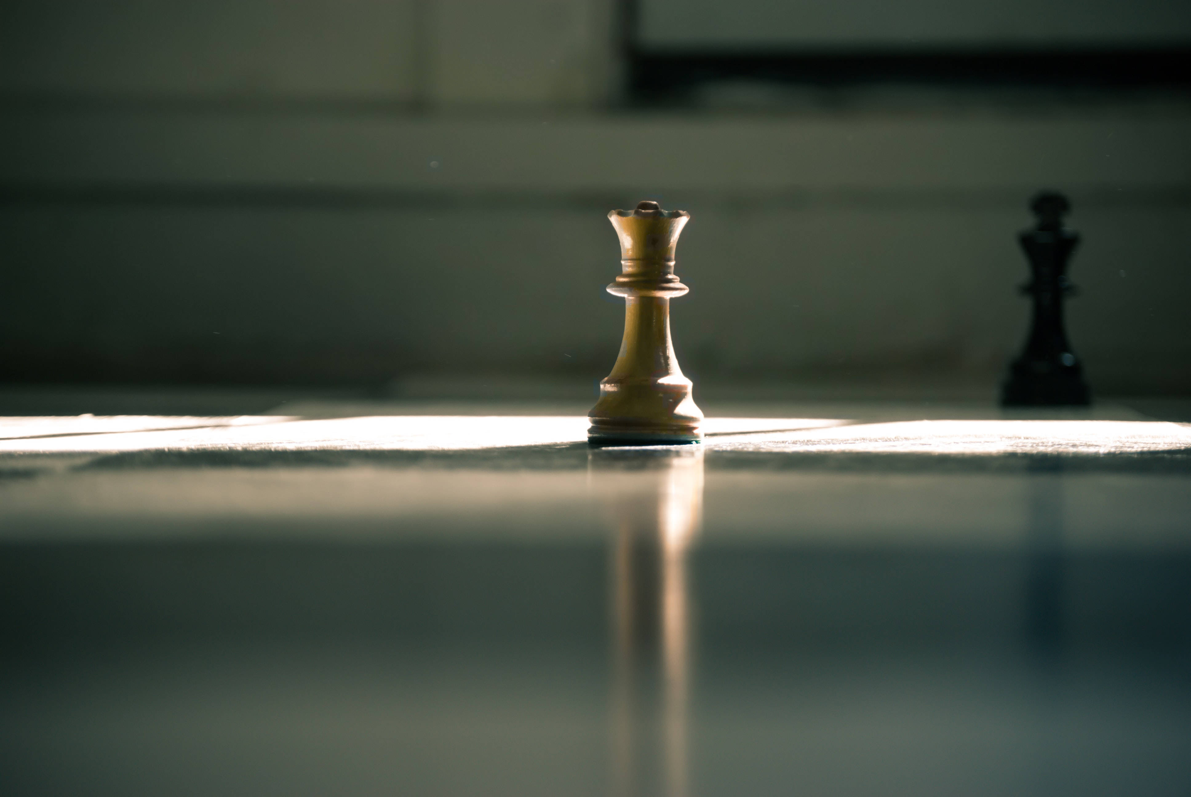遊戲 桌布 壁紙 — 一個金色的西洋棋國王站在反射的棋盤上，在溫暖的陽光下清晰對焦，背景中有一個模糊的深色對手棋子。