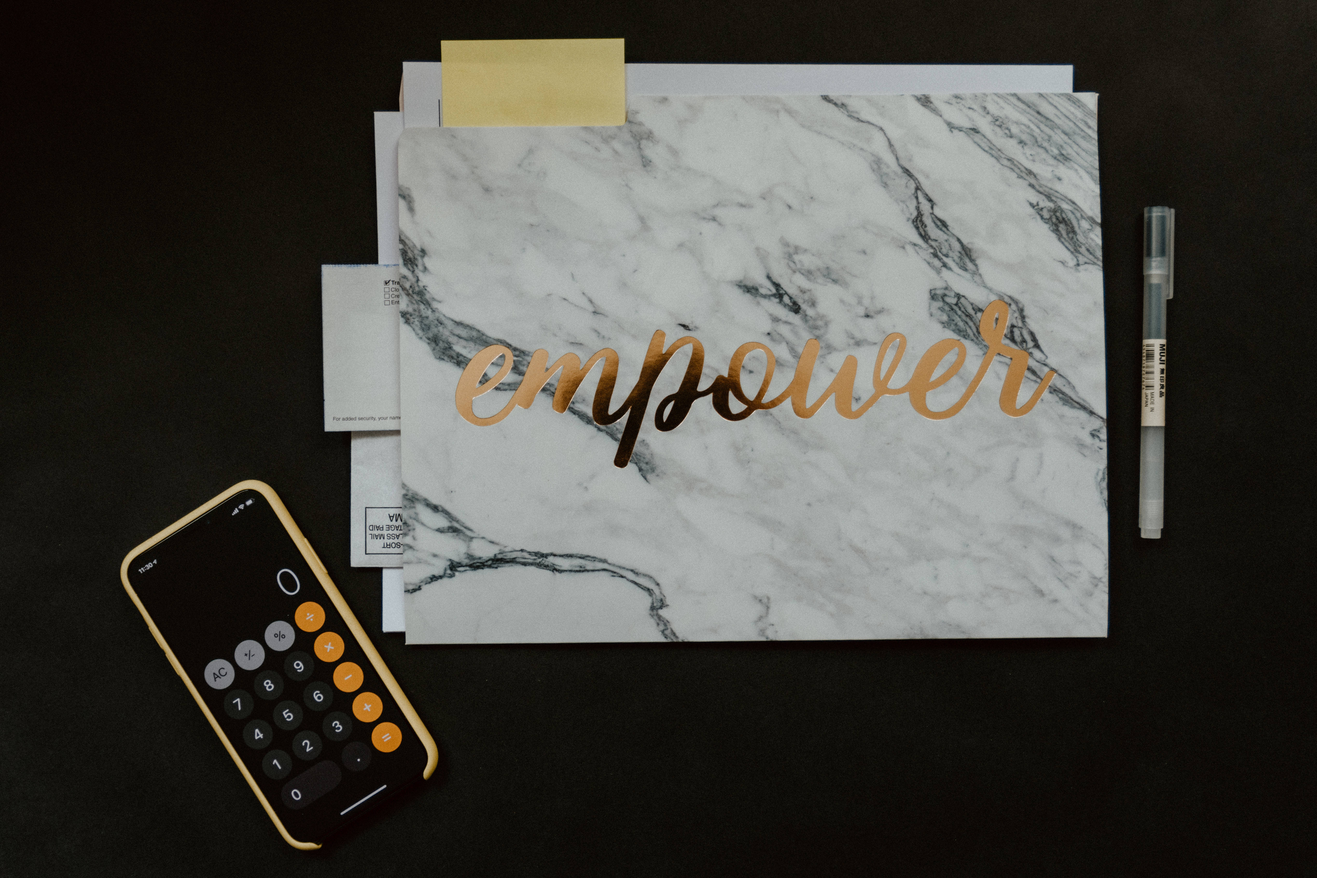 會計 桌布 壁紙 — 一個金色箔片 'empower' 字樣在白色大理石文件夾上，旁邊有計算機和筆在黑色表面上。