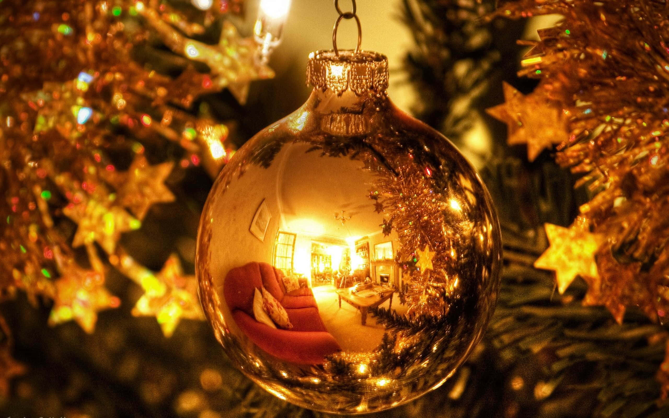 Gold Christmas 桌布 壁紙 — 一個金色聖誕裝飾反射出溫暖明亮的客廳，內有紅色沙發和節日燈飾，背景是模糊的聖誕樹。